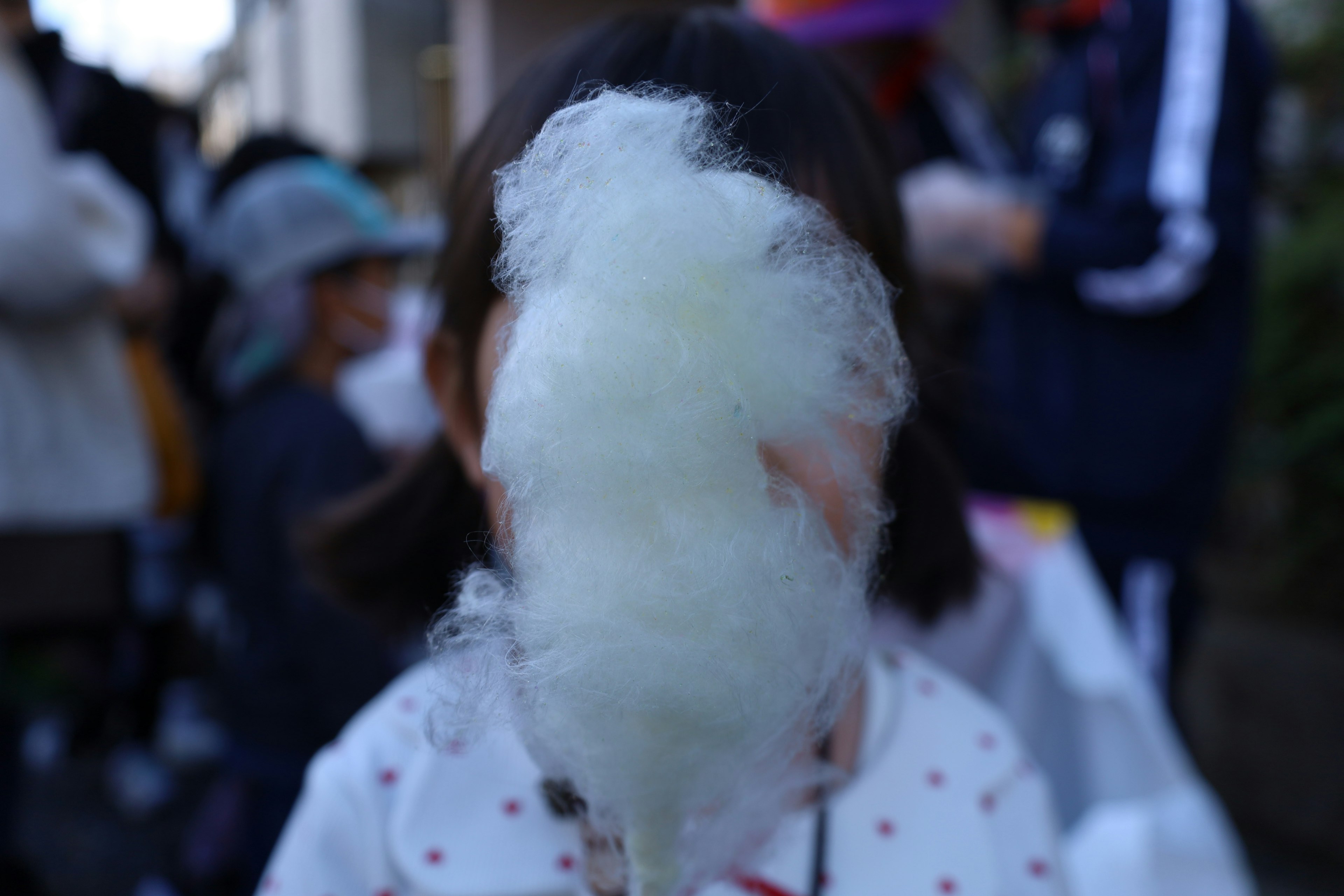 A child holding cotton candy obscuring their face with people in the background