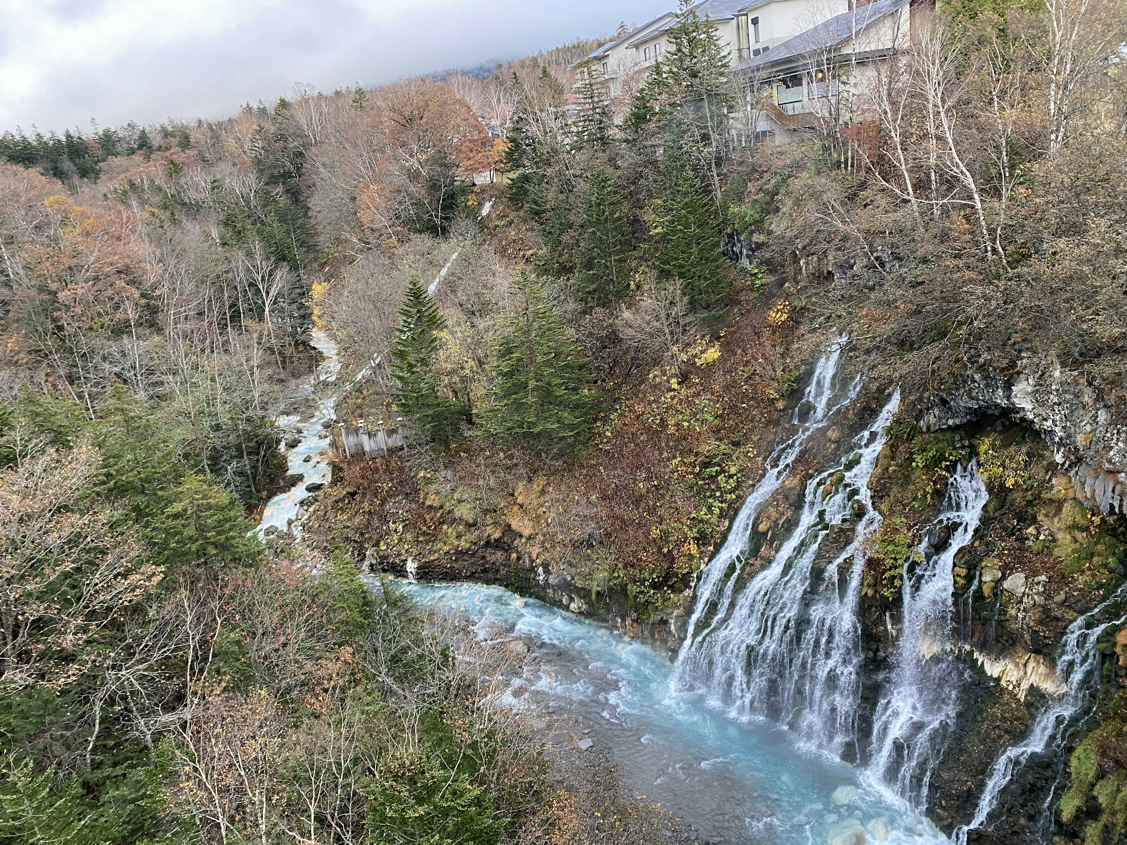 Scenic view of a waterfall cascading into a turquoise river surrounded by autumn trees