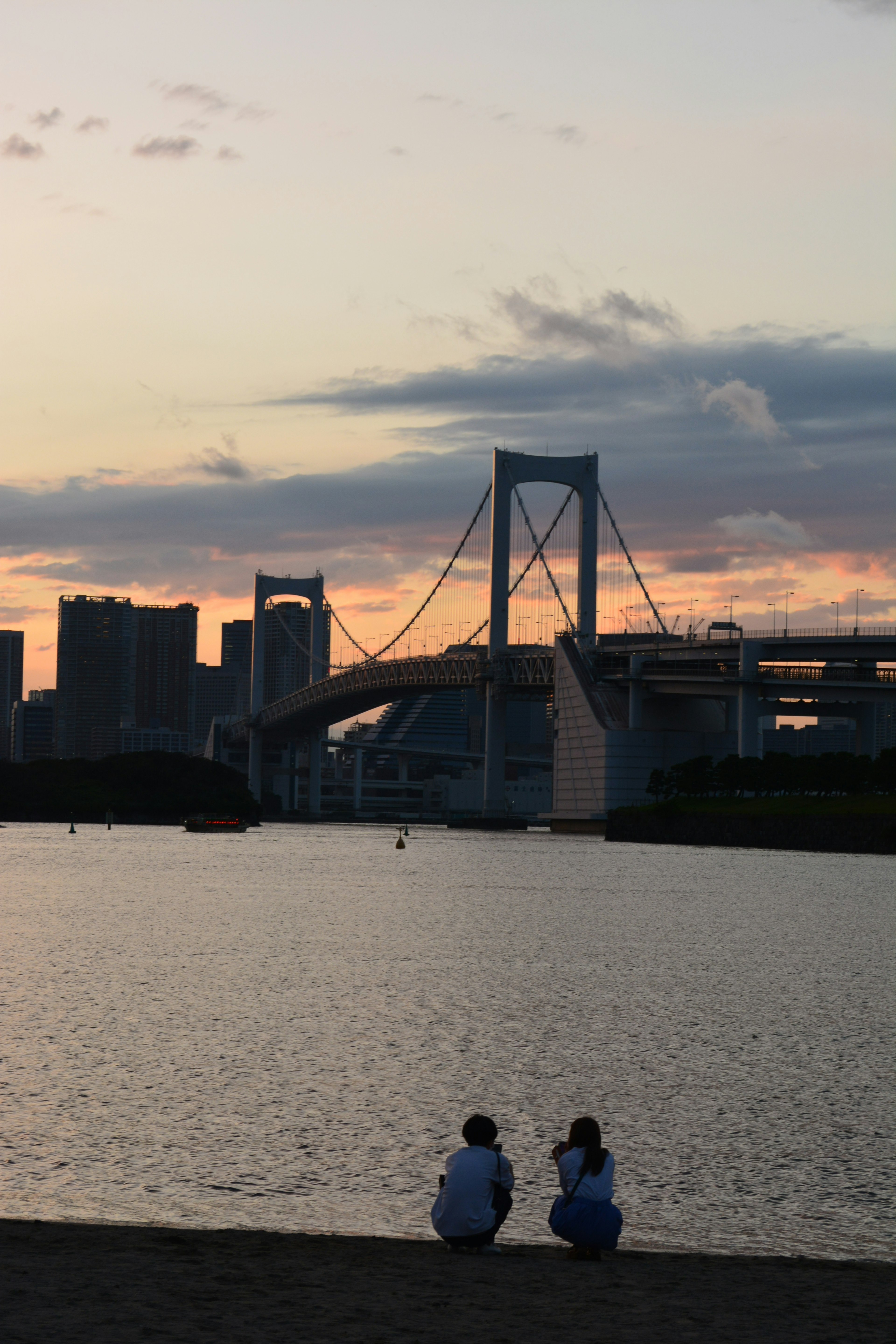 夕焼けの中でレインボーブリッジを背景に水辺に座る二人