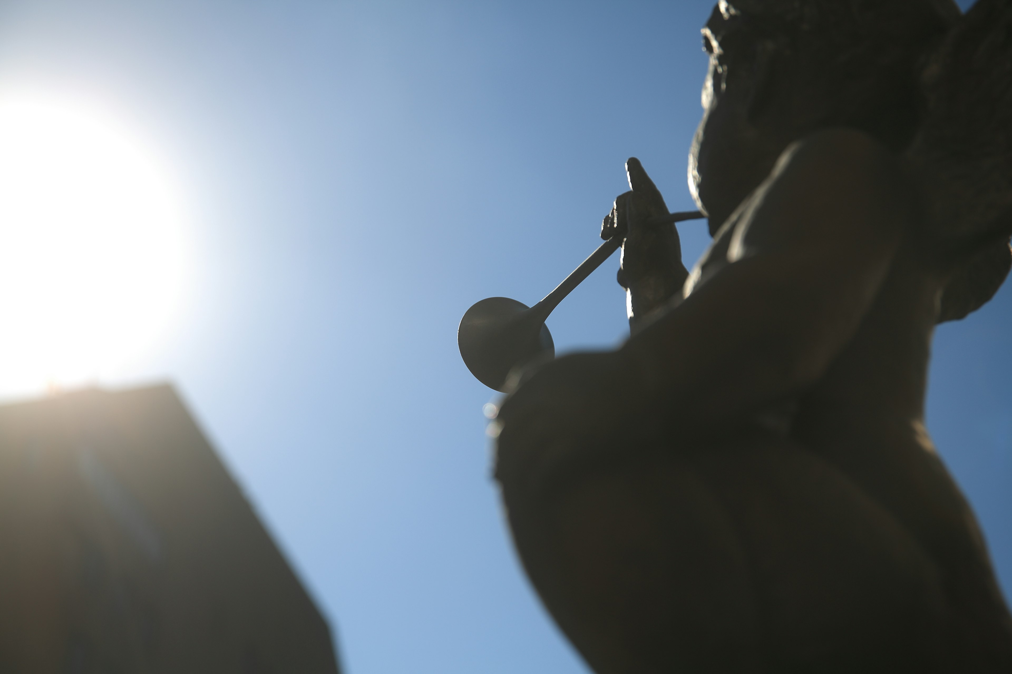 Silhouette of an angel sculpture holding an instrument under a blue sky