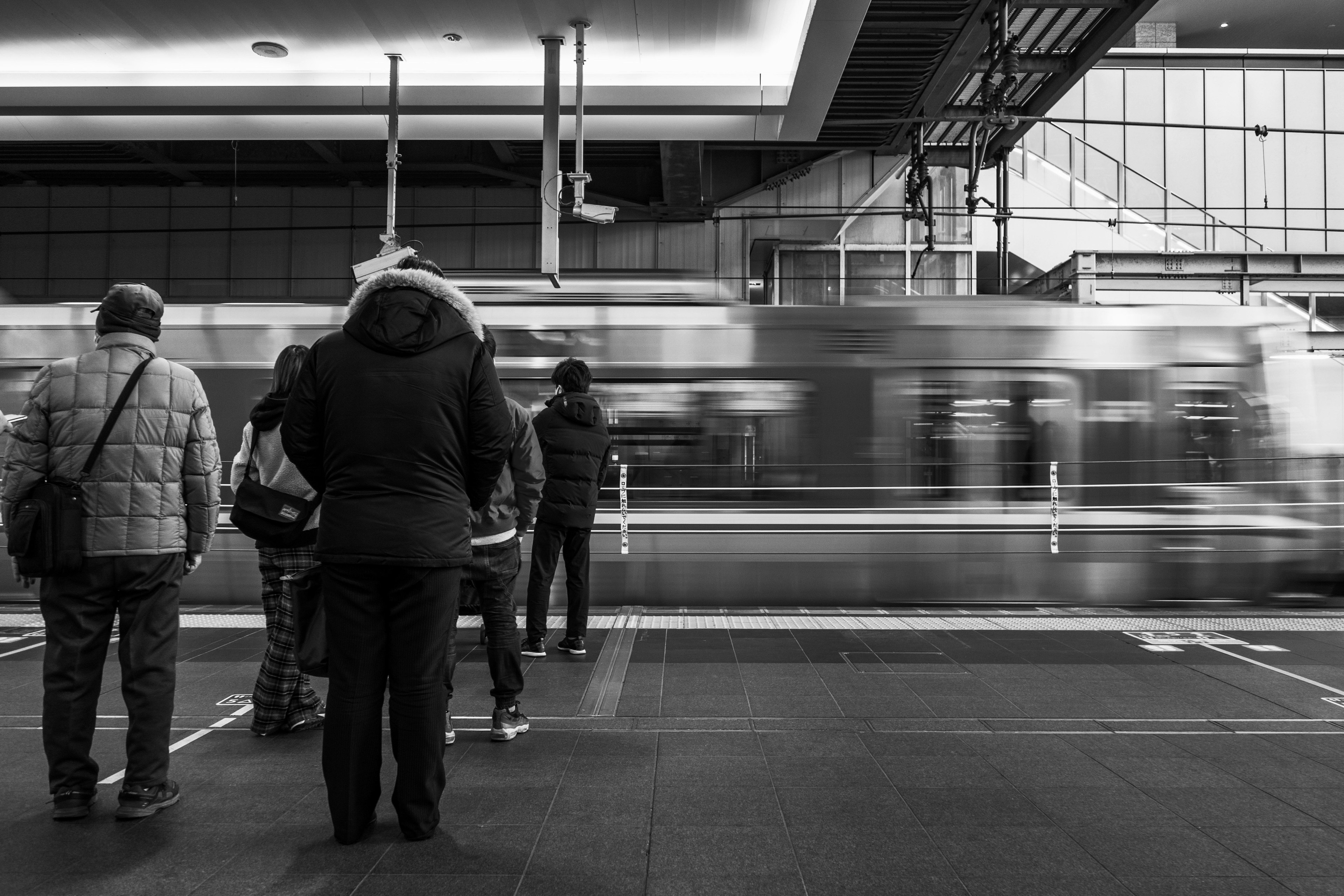 Silhouetten von Menschen, die an einer Station warten, mit einem verschwommenen Zug in Bewegung