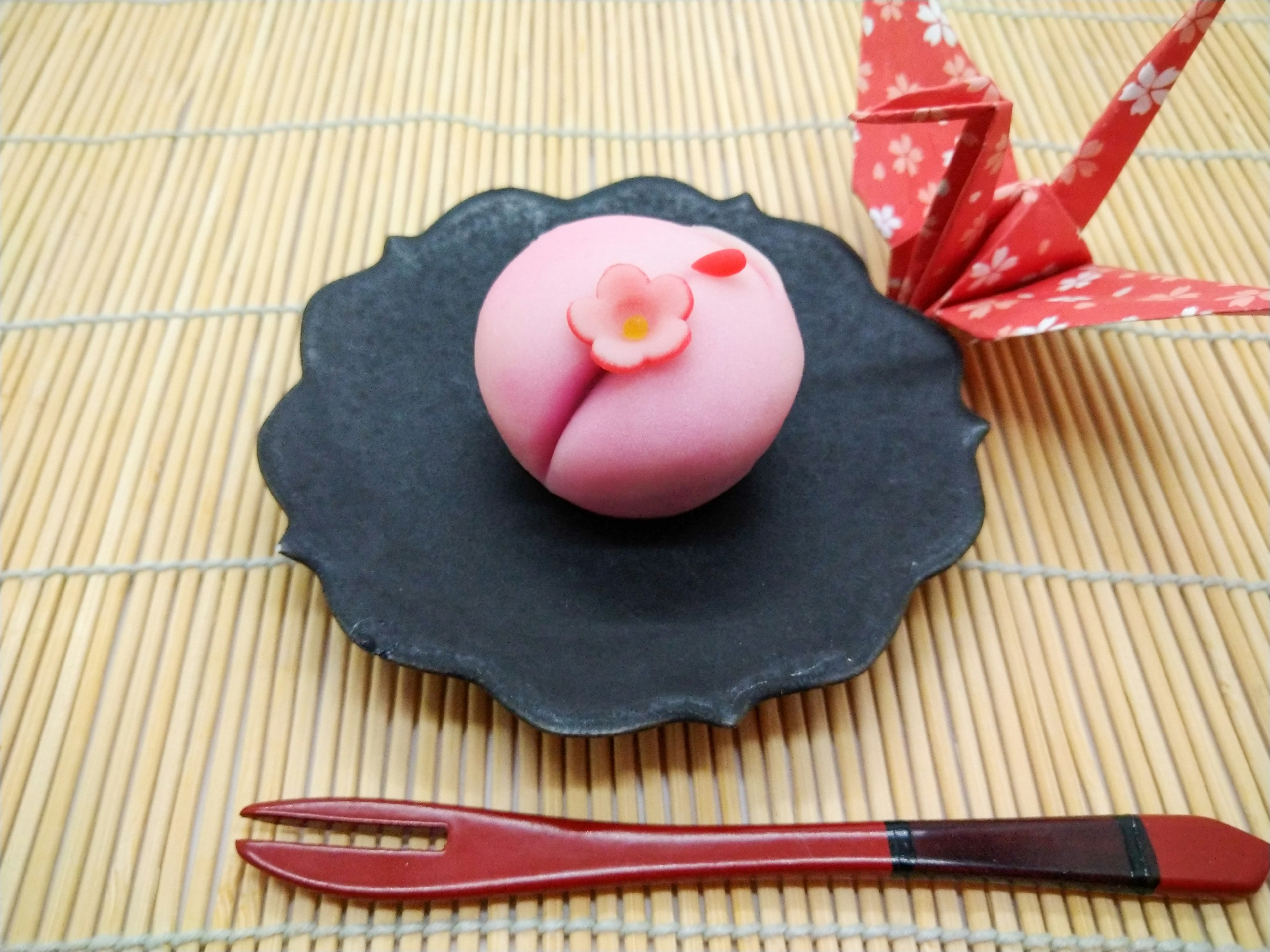 Dulce japonés rosa en un plato negro con una grulla de origami roja