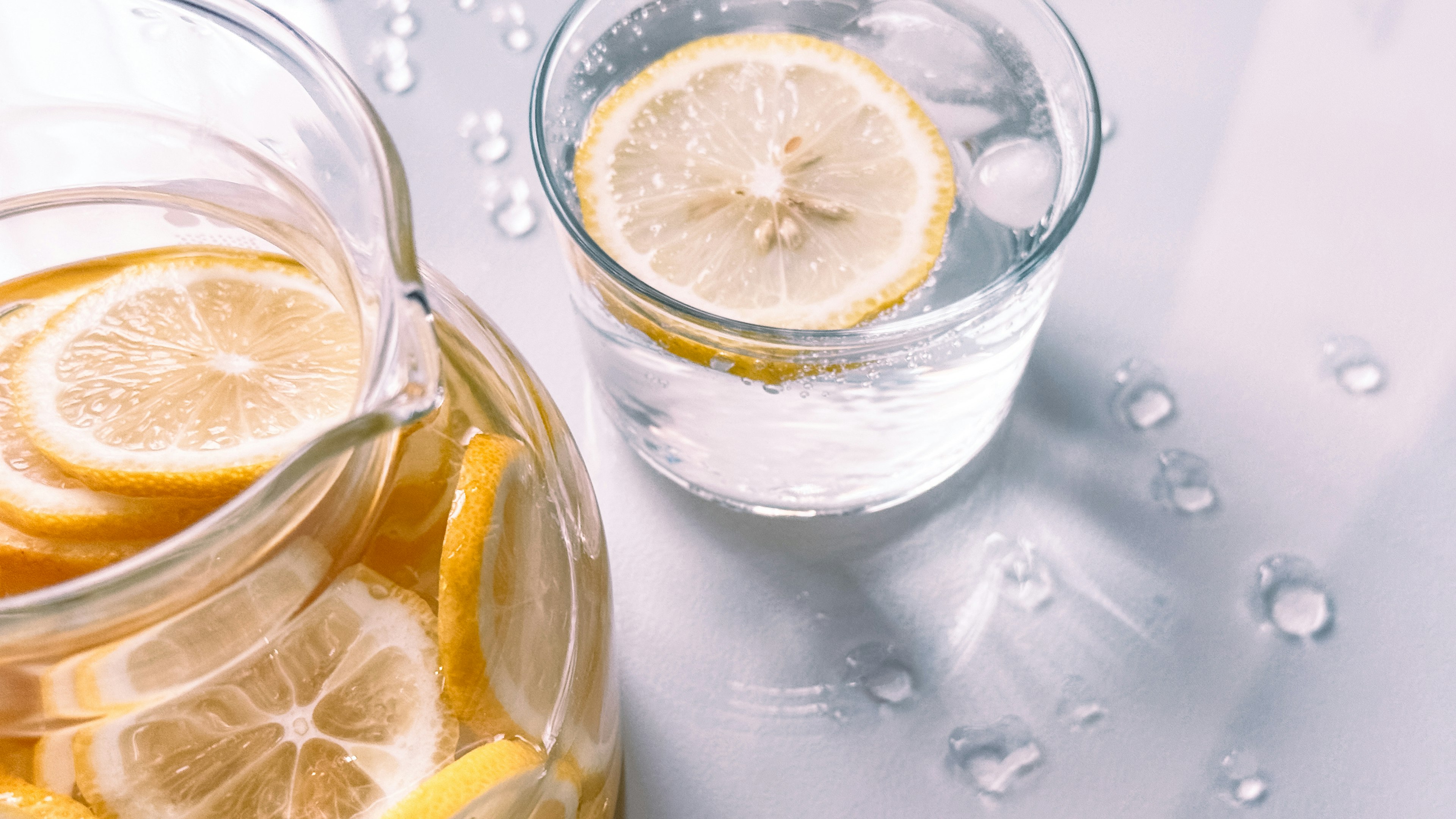 A pitcher of lemon water and a glass with lemon slices floating in it