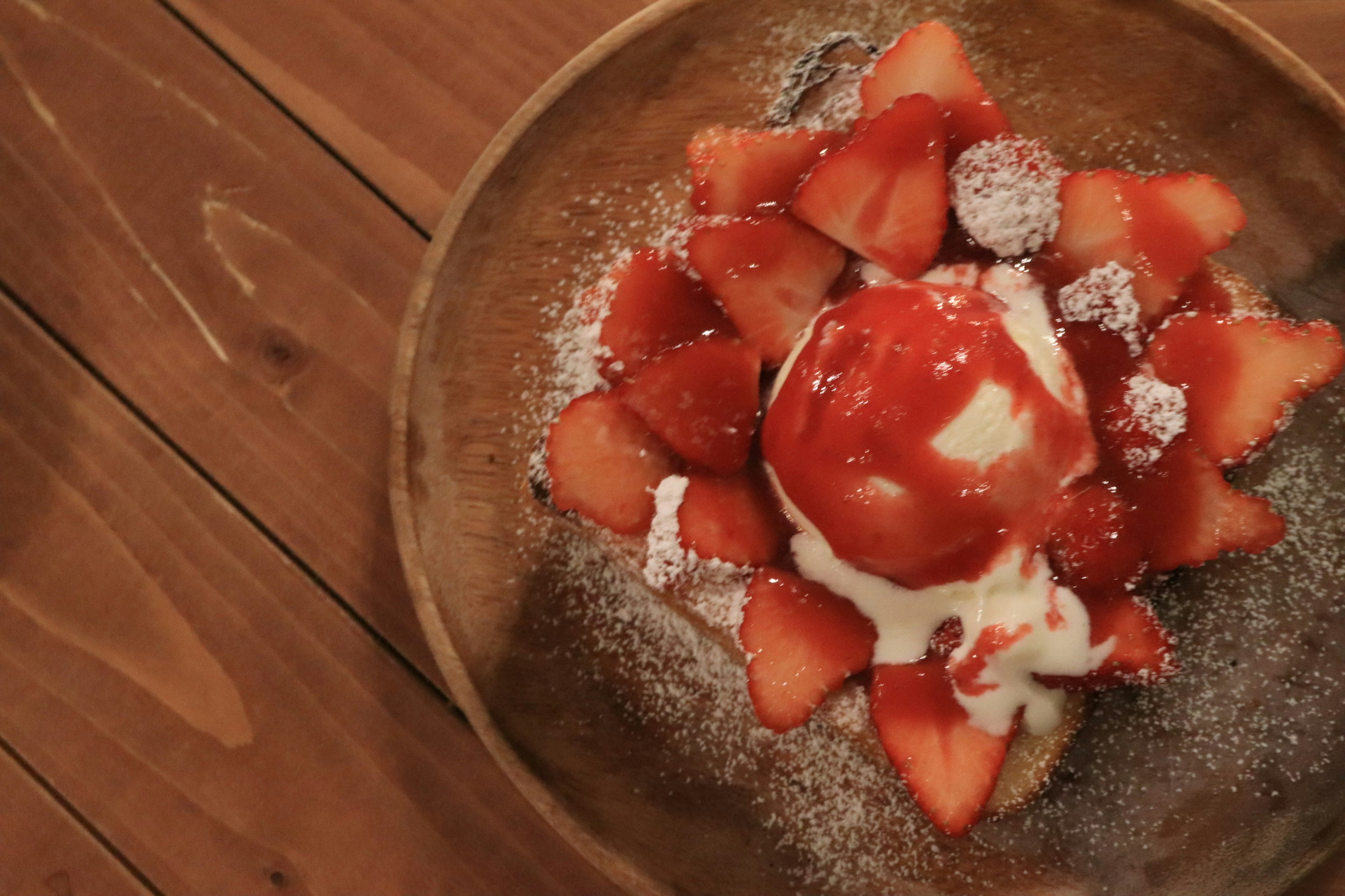 Dessert avec des fraises et de la glace servi dans une assiette en bois