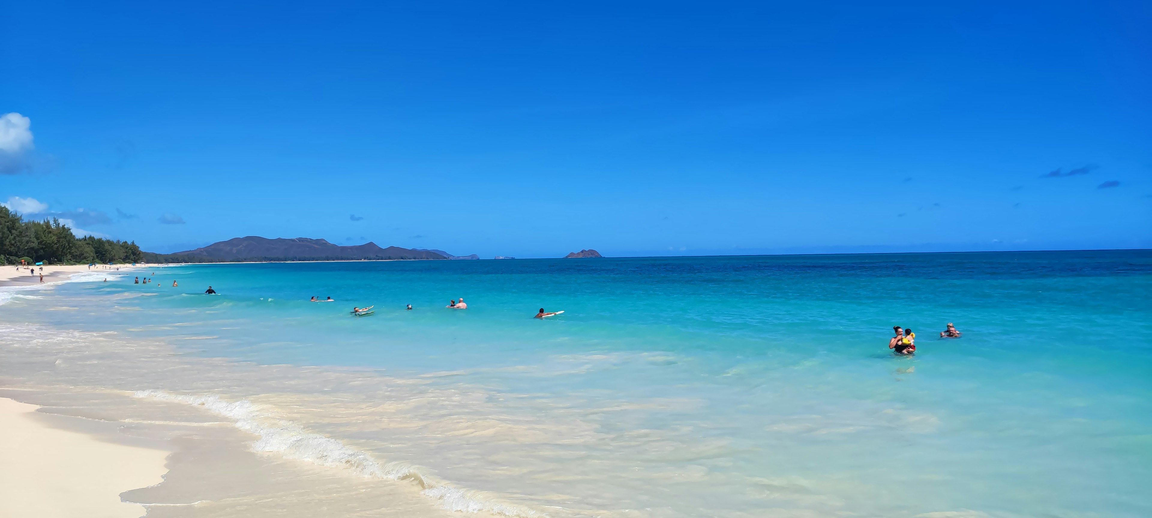 Scenic beach with turquoise water and white sand featuring people swimming