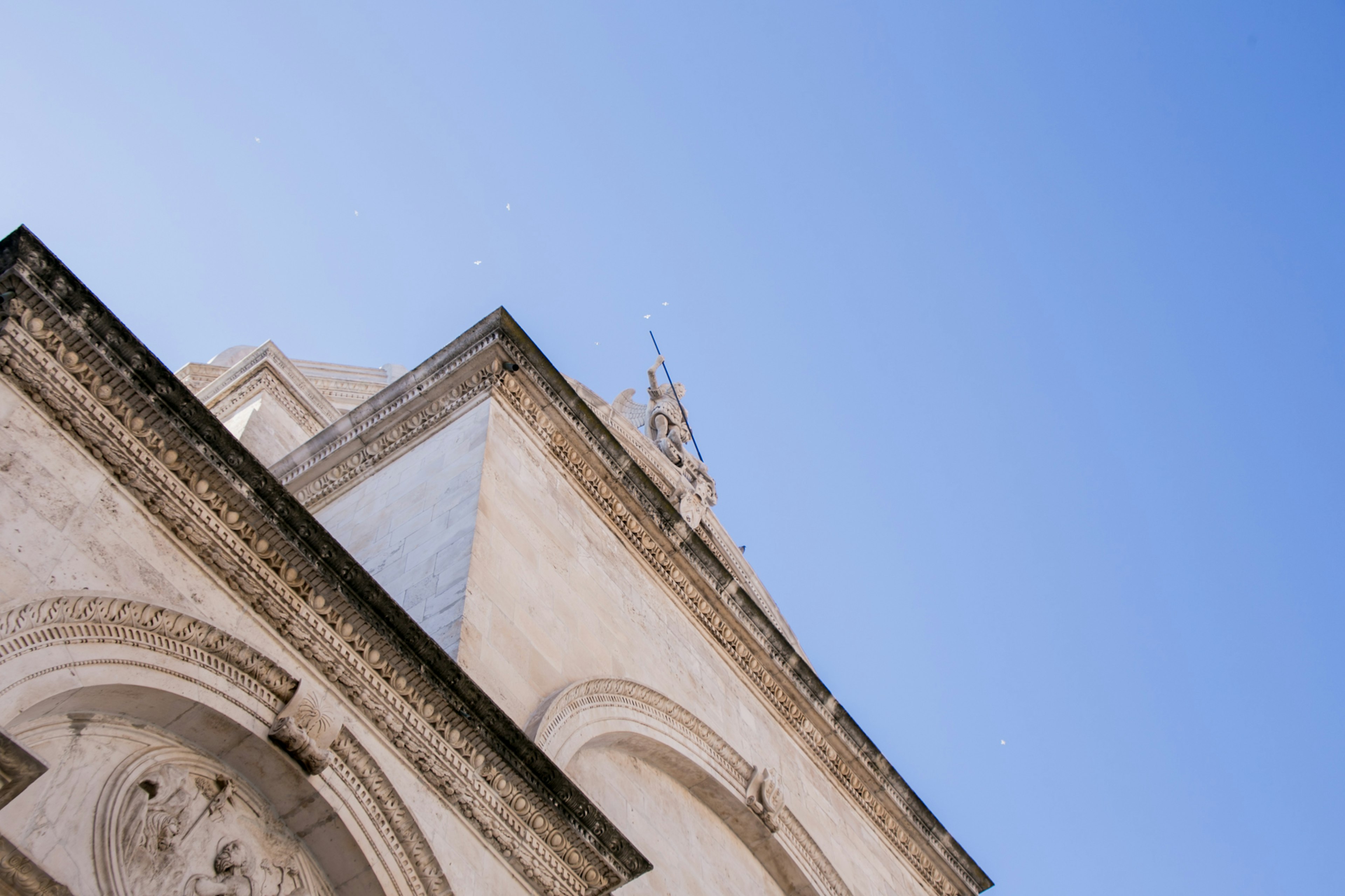 Photo d'un bâtiment vu d'un angle ascendant sous un ciel bleu avec des murs extérieurs lumineux et des éléments décoratifs