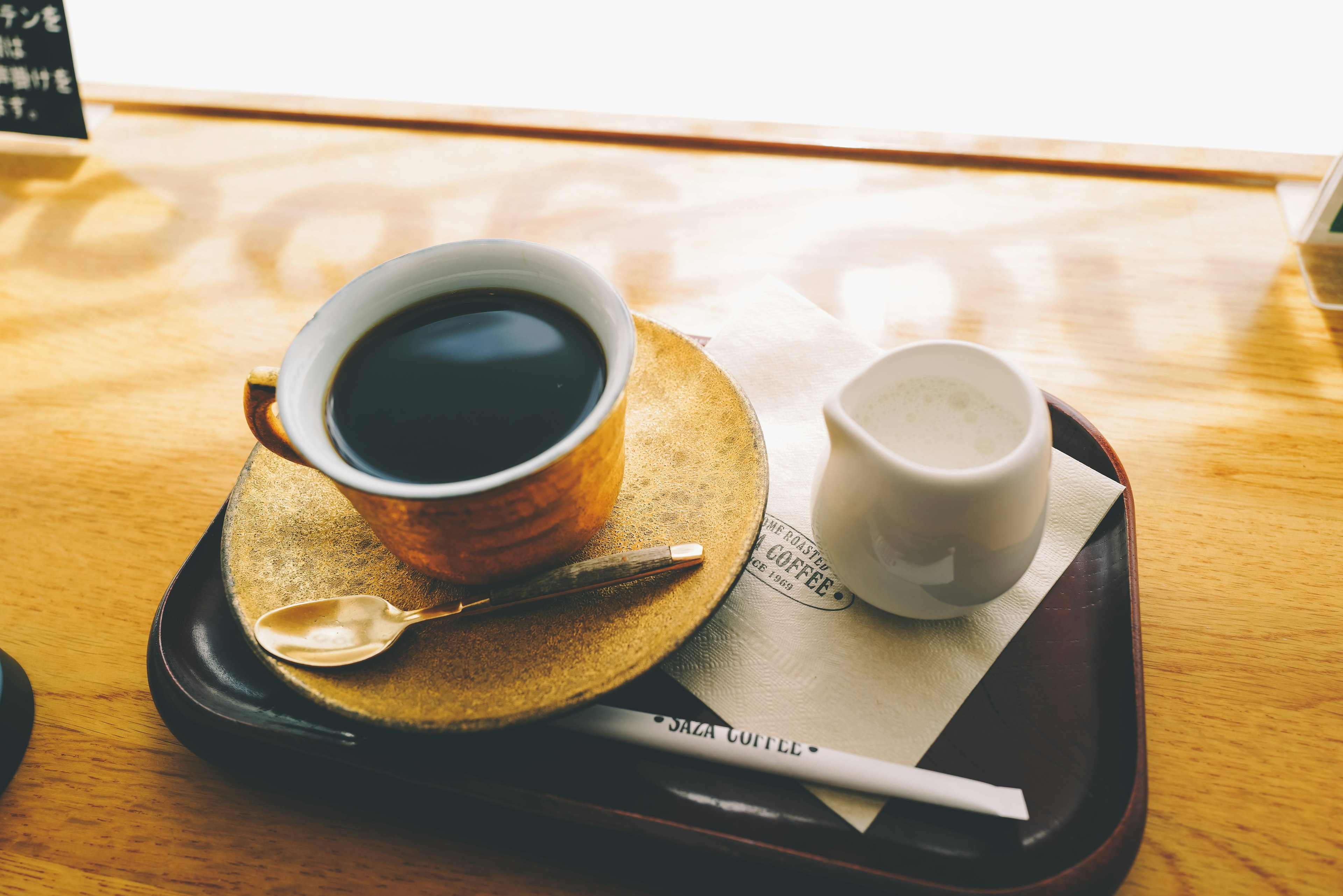 A coffee cup and cream on a tray with a spoon and napkin