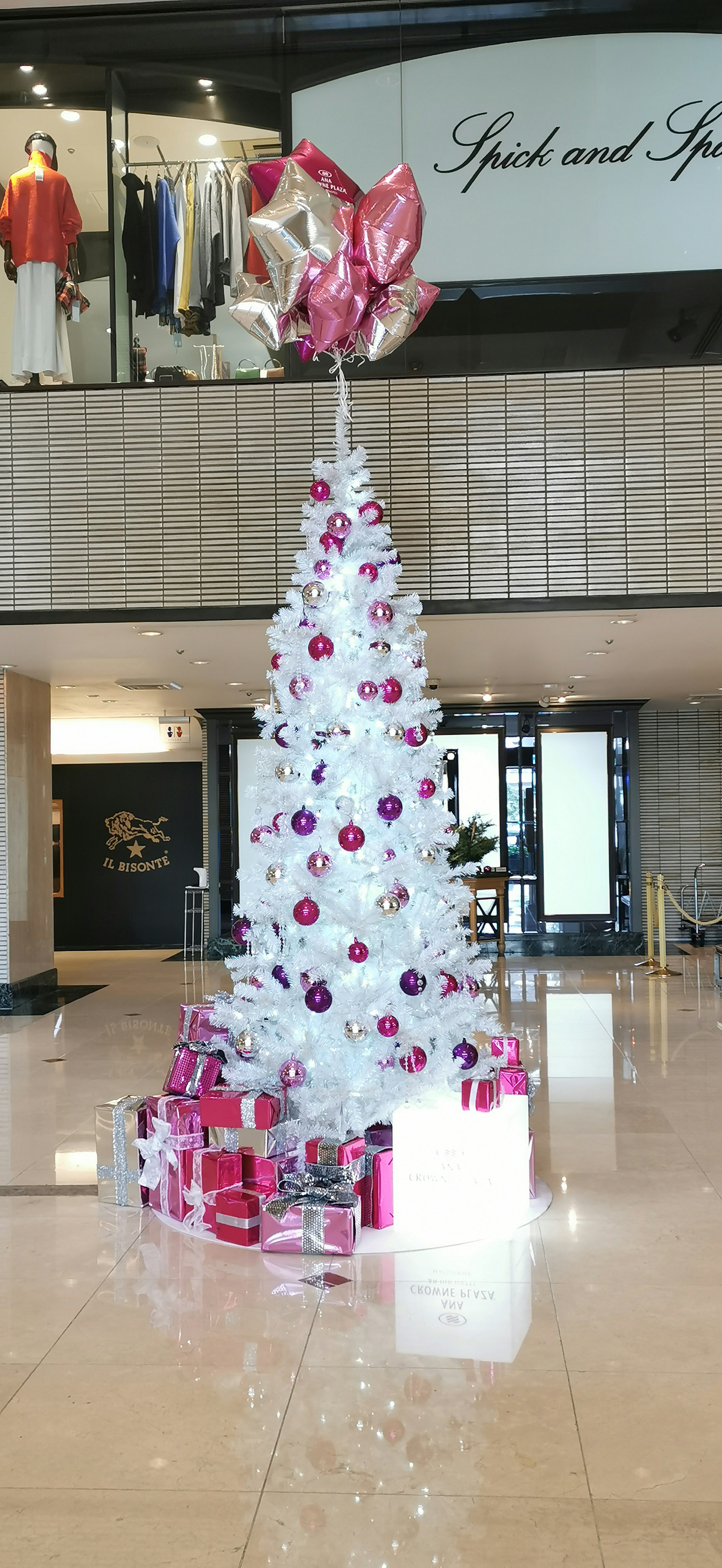 White Christmas tree adorned with pink and purple ornaments surrounded by gift boxes