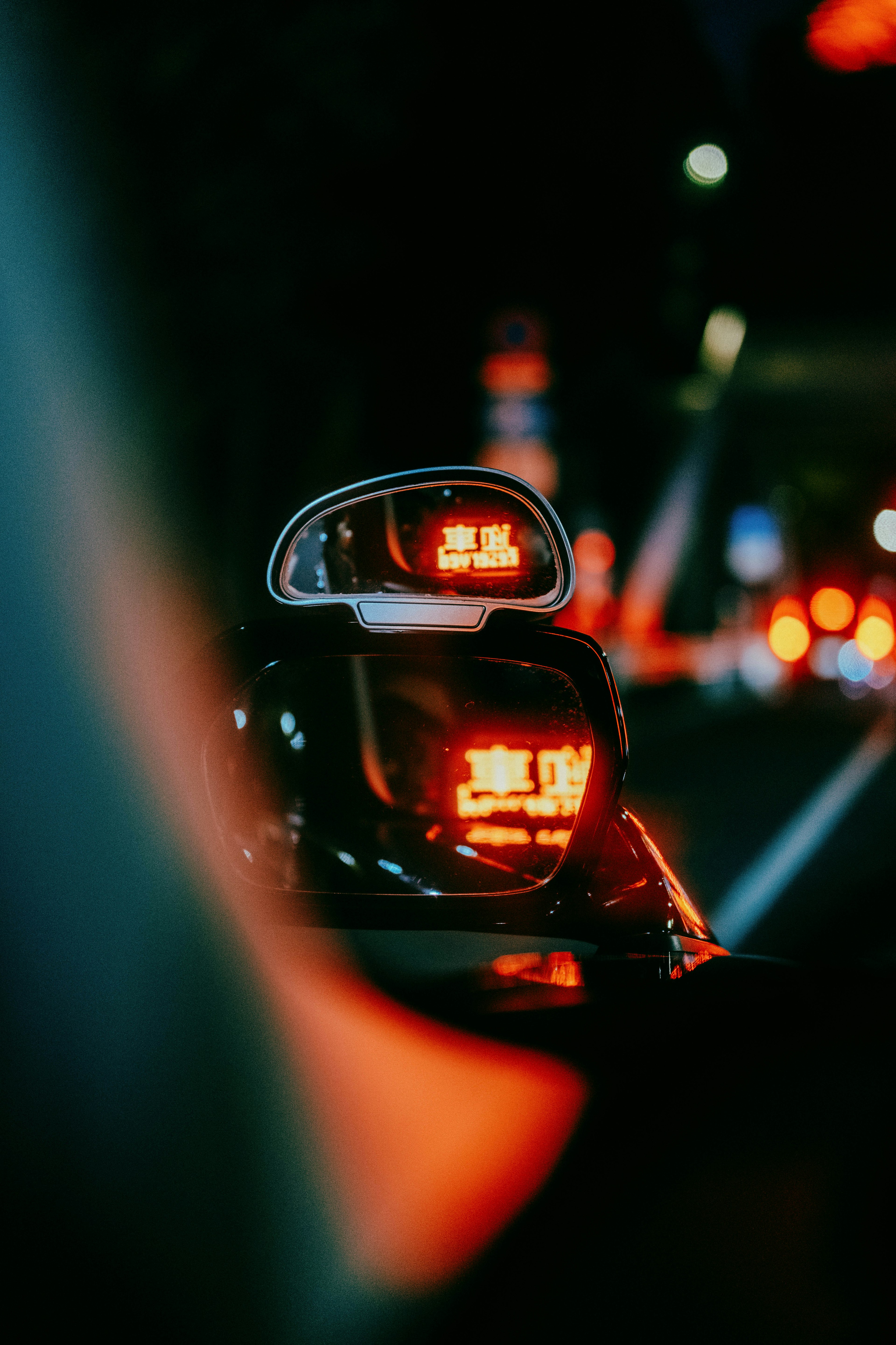 Taxi side mirror reflecting red lights in a night city setting