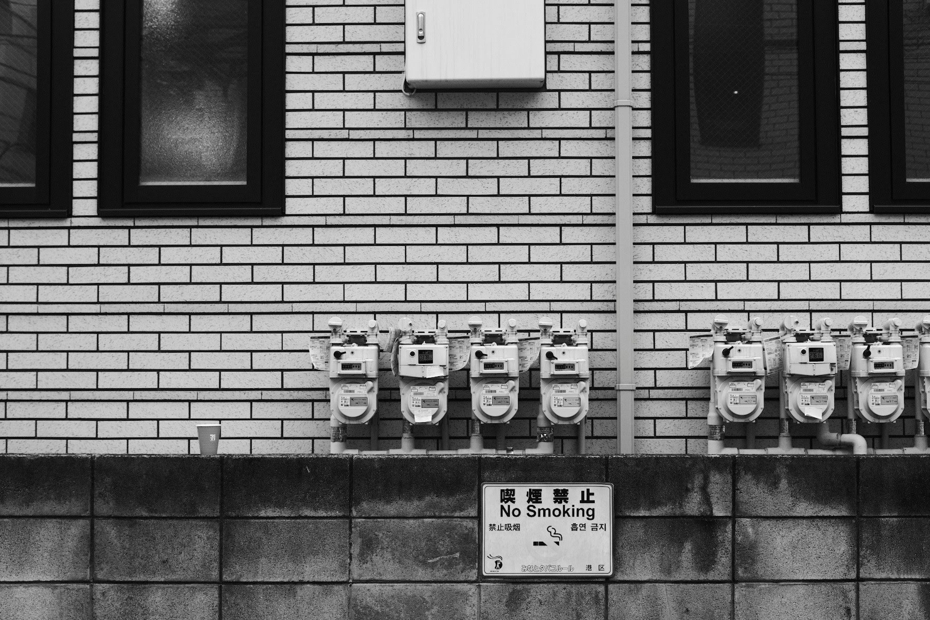 Multiple gas meters mounted on a brick wall with windows in black and white