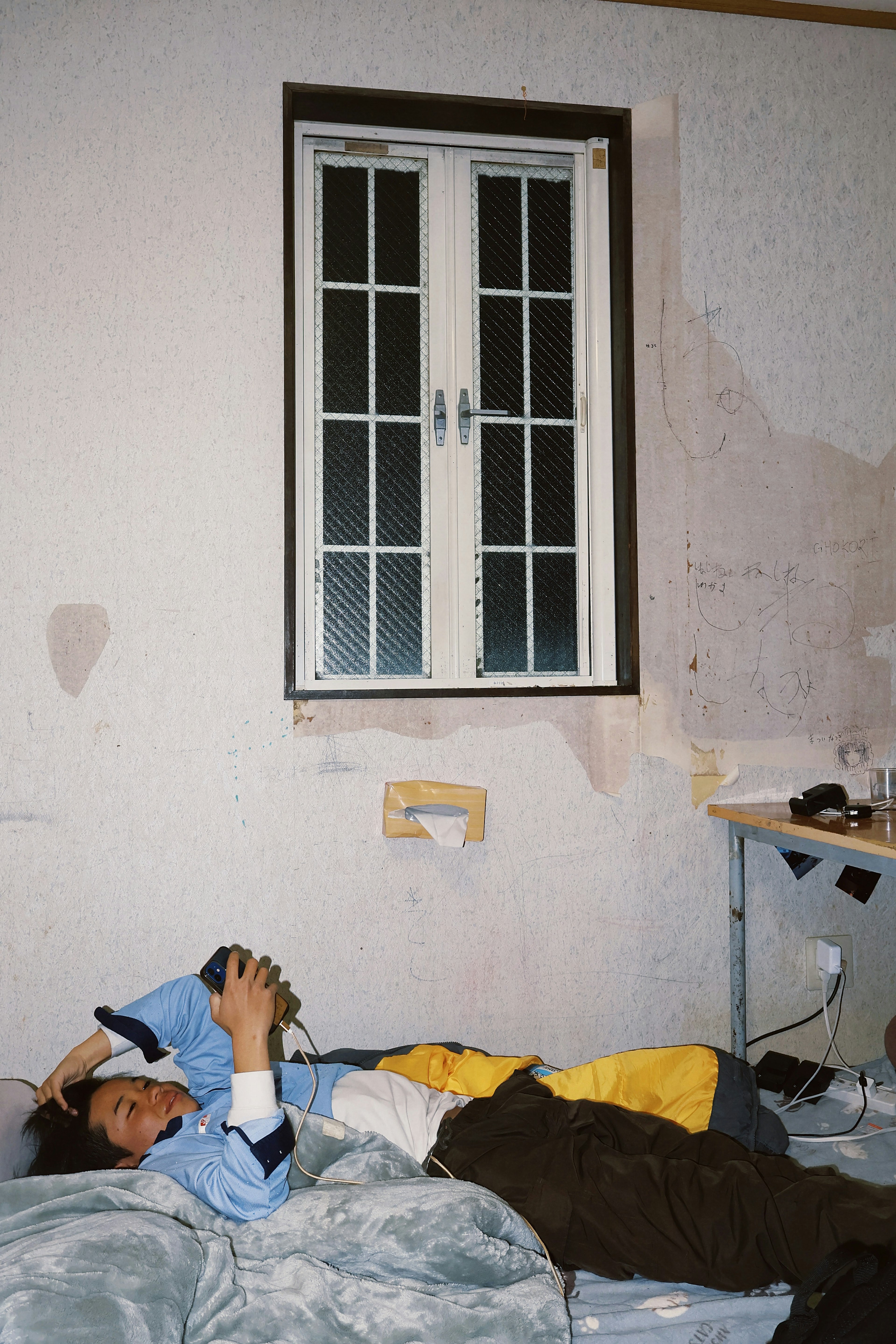 Un hombre durmiendo en una cama con una ventana visible y manchas en la pared