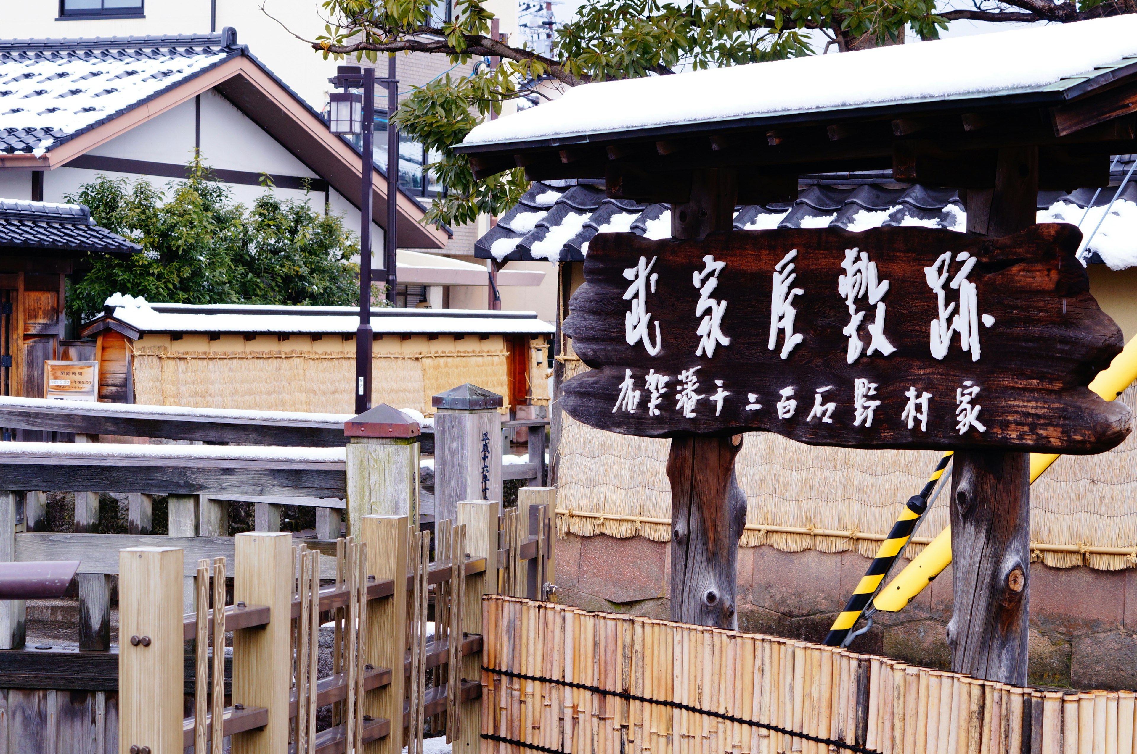 Cartel de madera frente a edificios japoneses tradicionales cubiertos de nieve