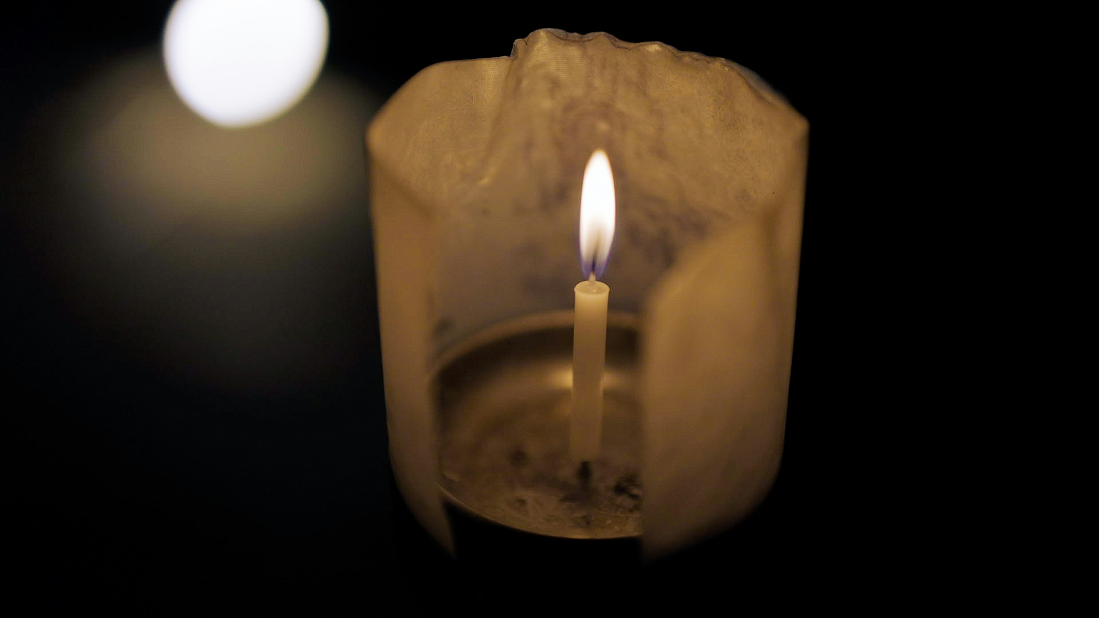 A bright candle flame in a dark setting with a soft glowing light in the background