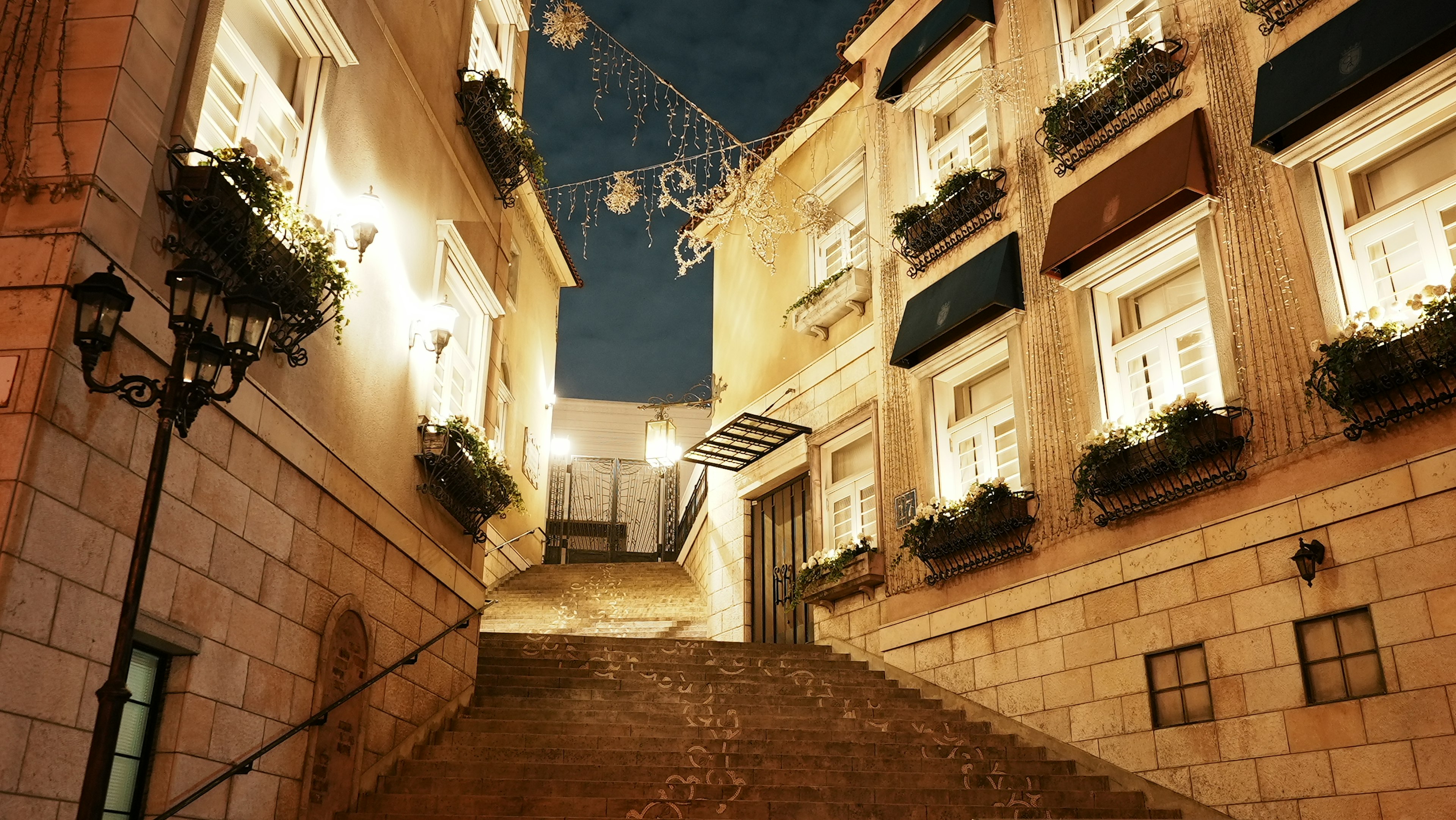 Beleuchtete Treppe in einer malerischen Gasse mit Blumenkästen bei Nacht