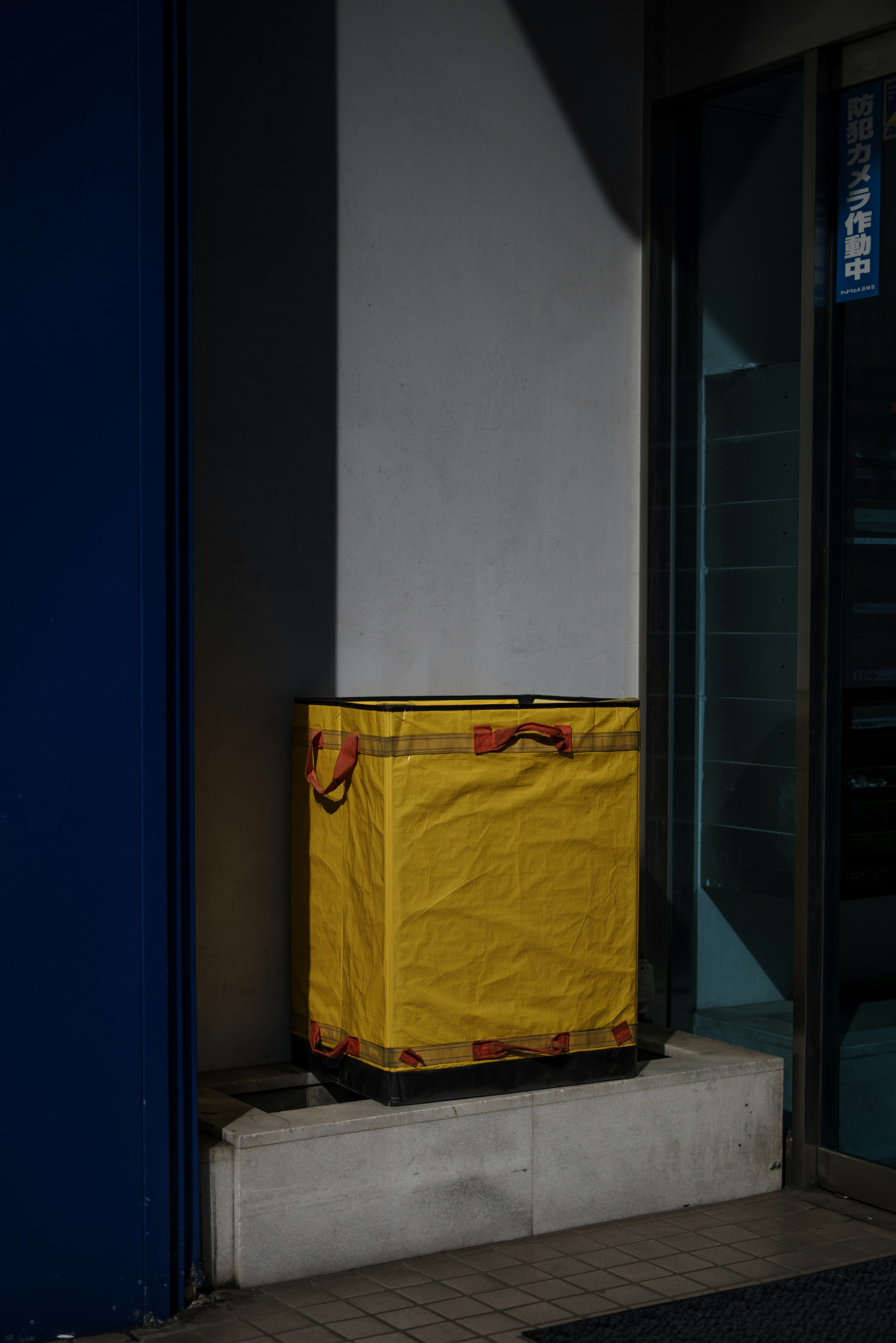 A trash bin covered with a yellow tarp placed in a corner against a wall