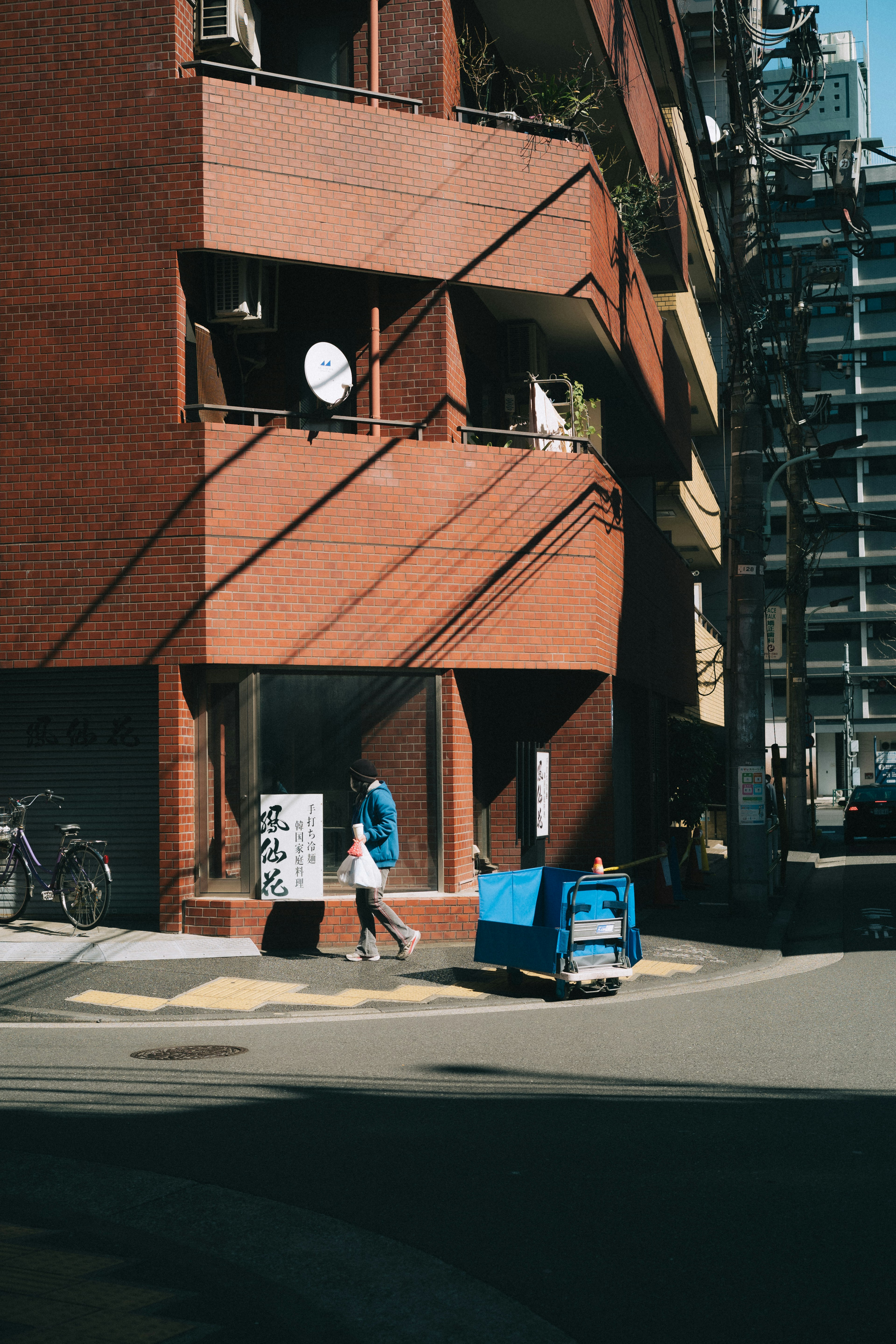 Escena urbana con una persona en la esquina de un edificio de ladrillo rojo y un carrito azul