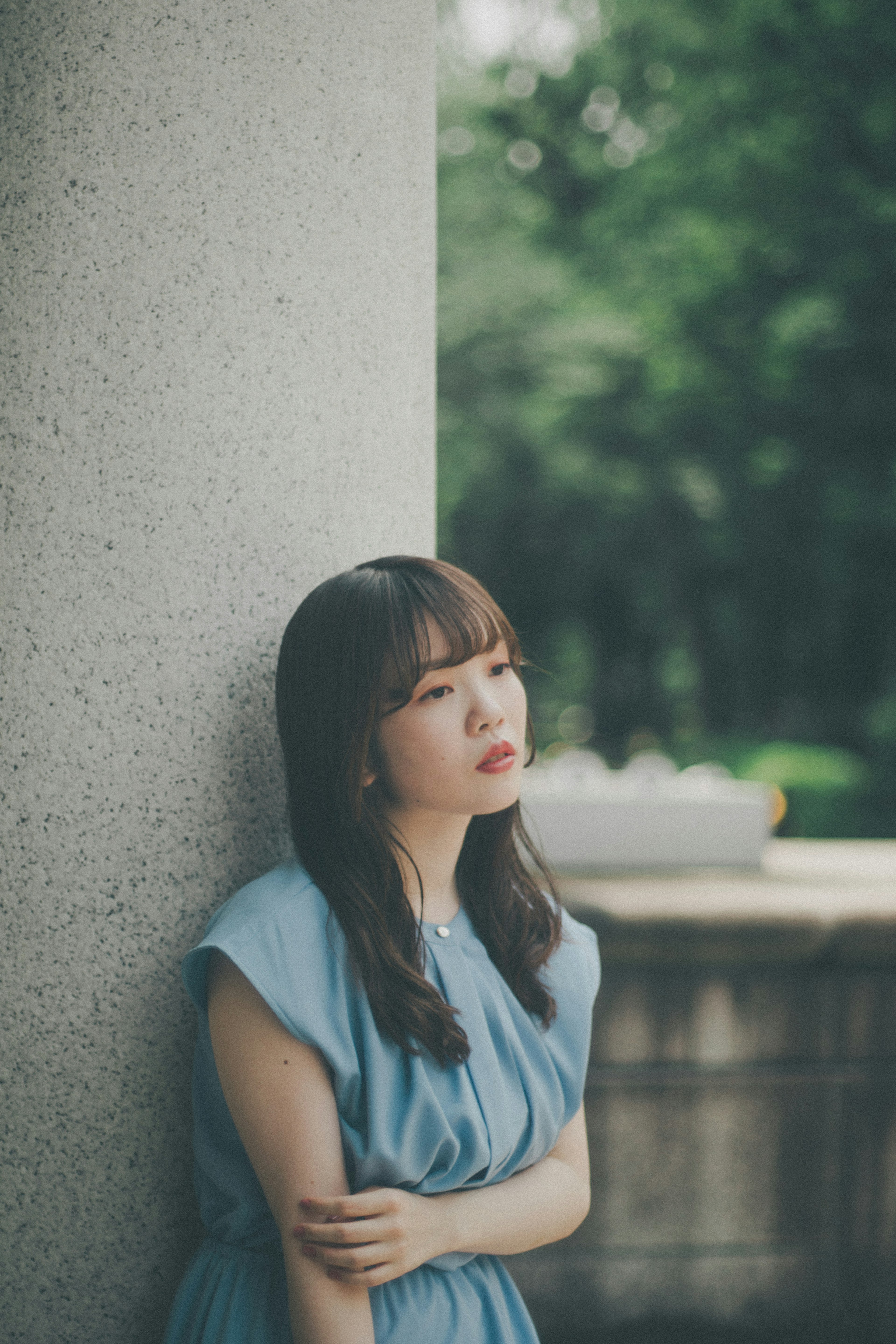 A woman in a blue dress leans against a pillar looking contemplative