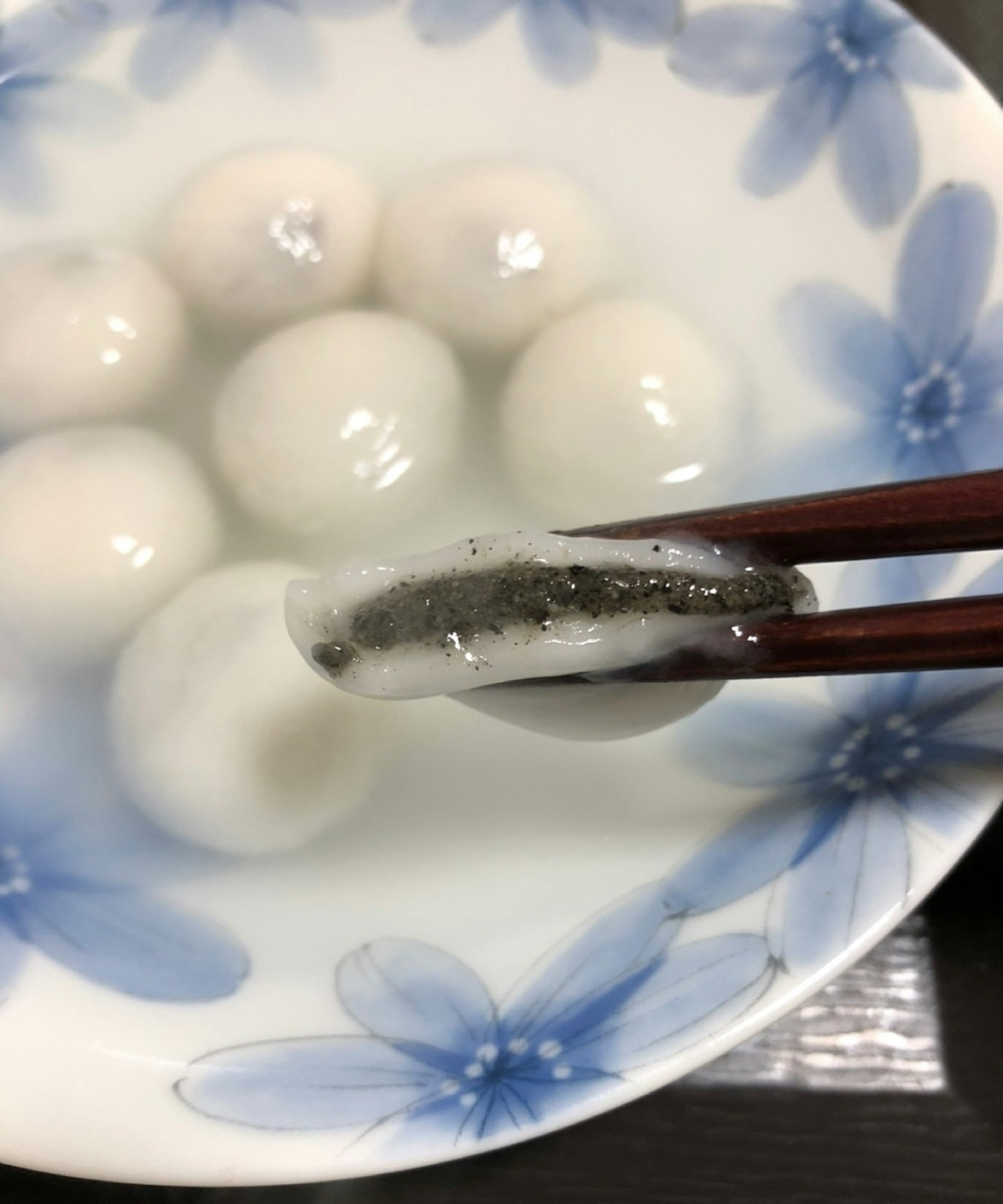 Stäbchen halten einen Dumpling mit schwarzer Füllung zwischen weißen Dumplings