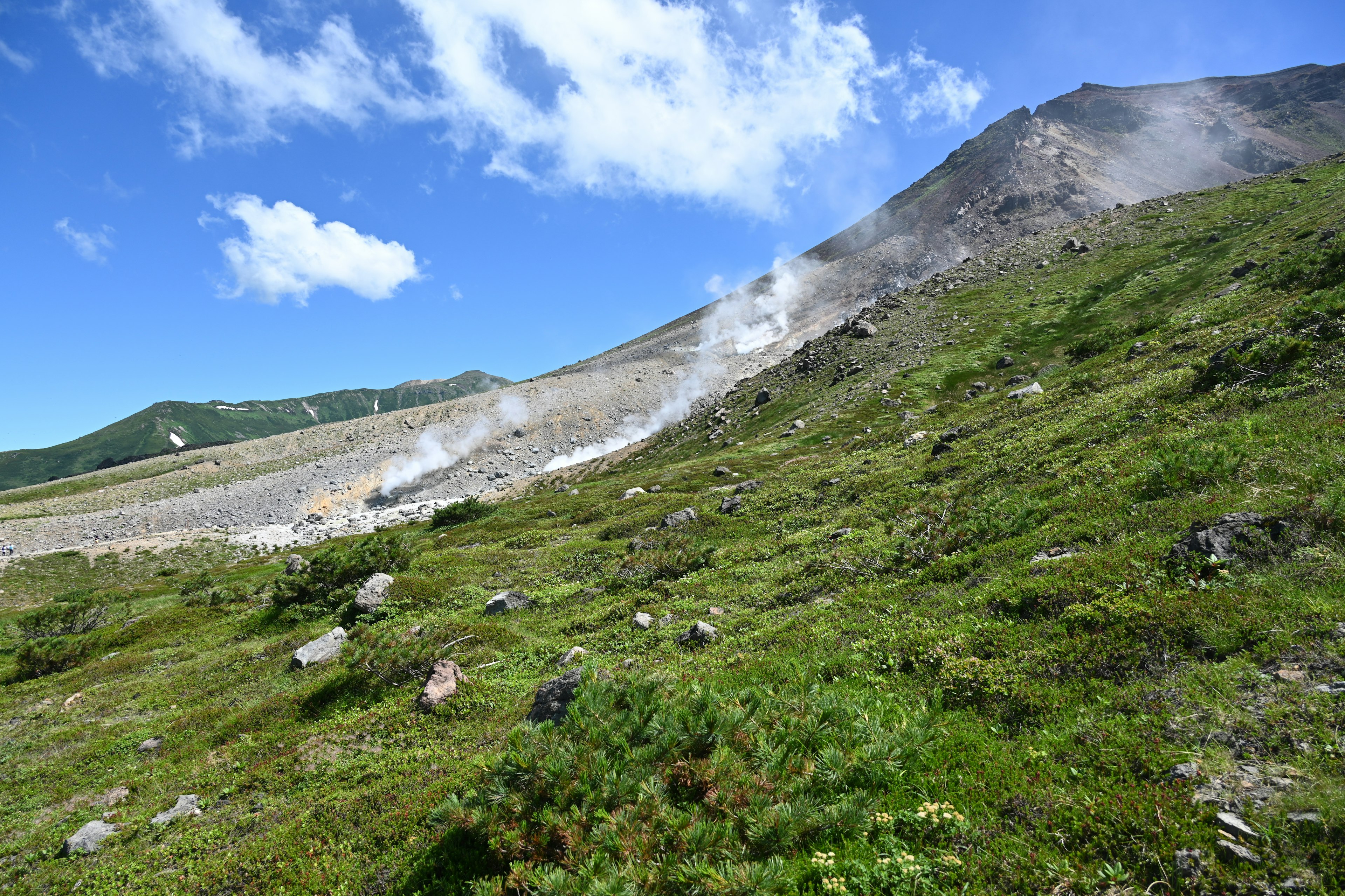 A hillside with smoke rising green grass and a clear blue sky