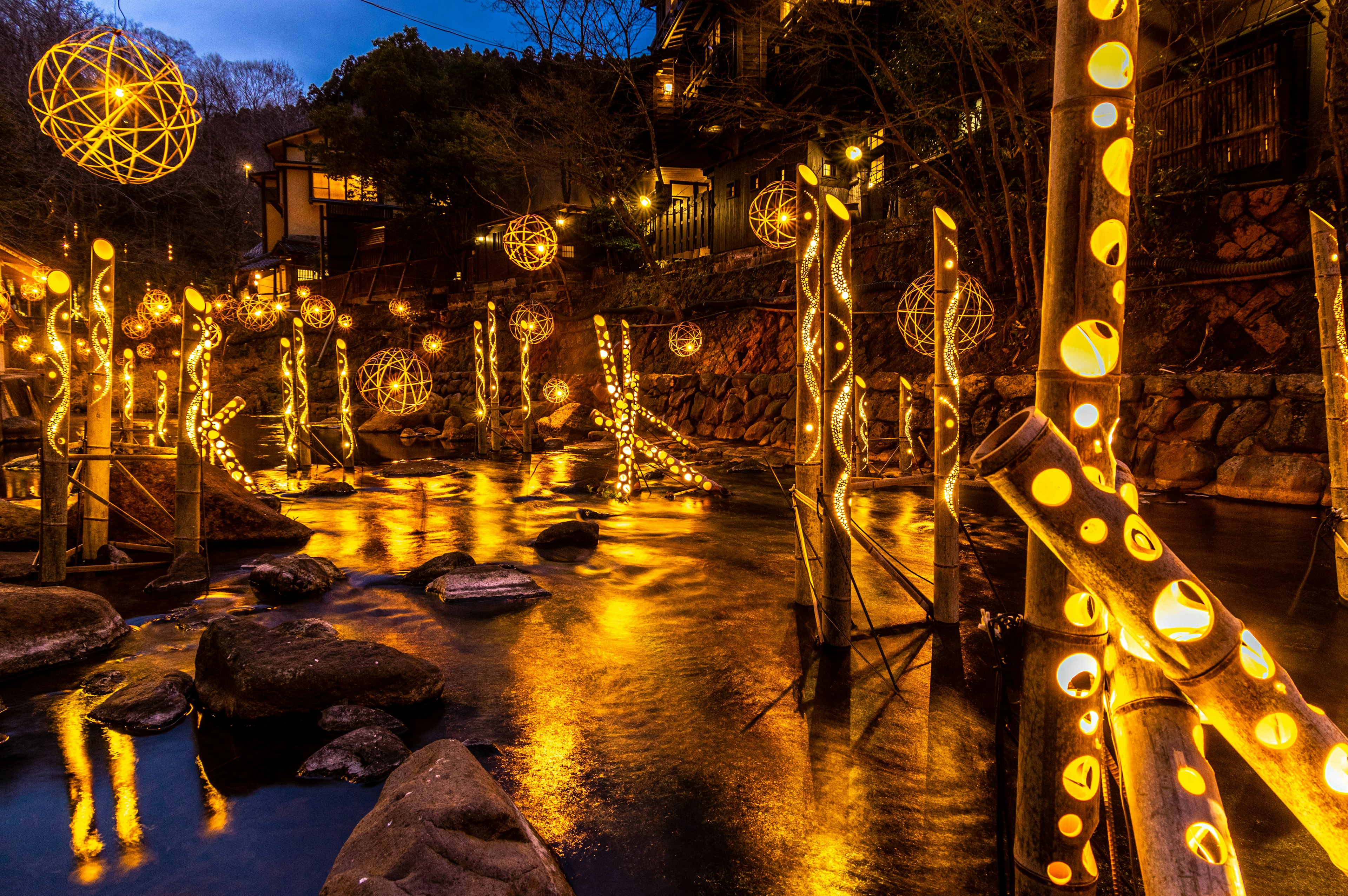 Glowing lanterns along a riverside at night reflecting in the water