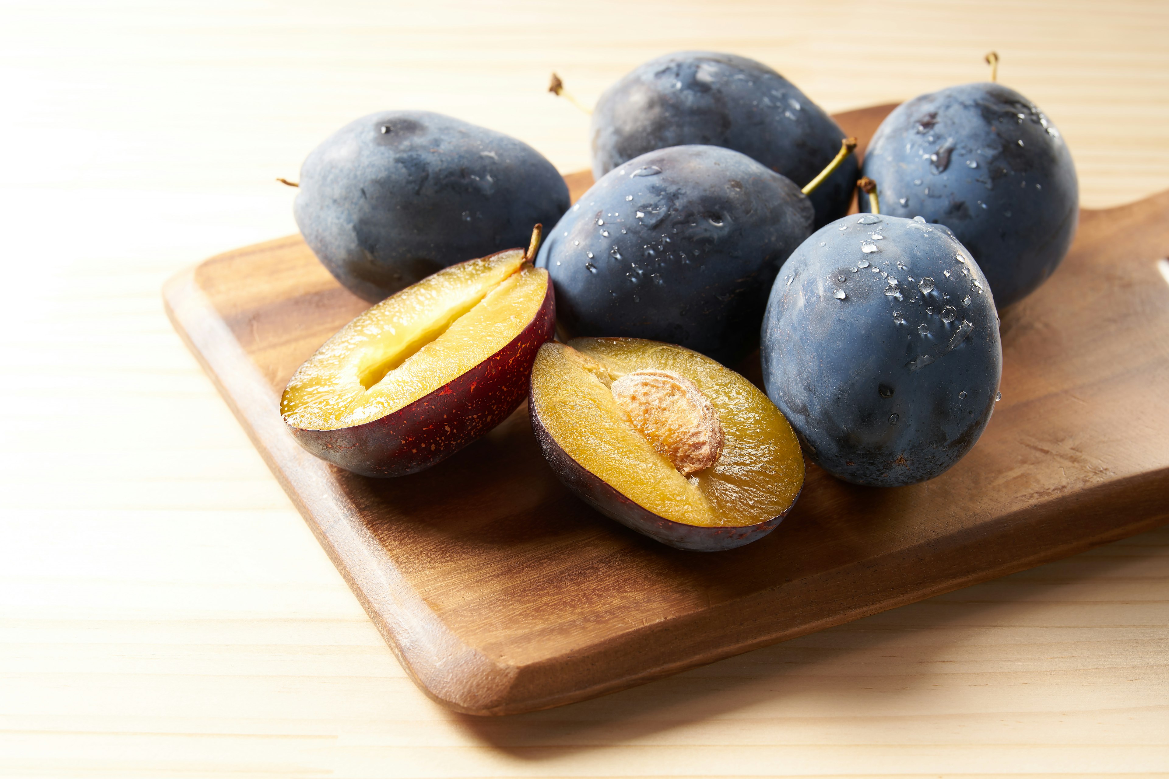 Prunes bleues sur une planche en bois avec une coupée en deux