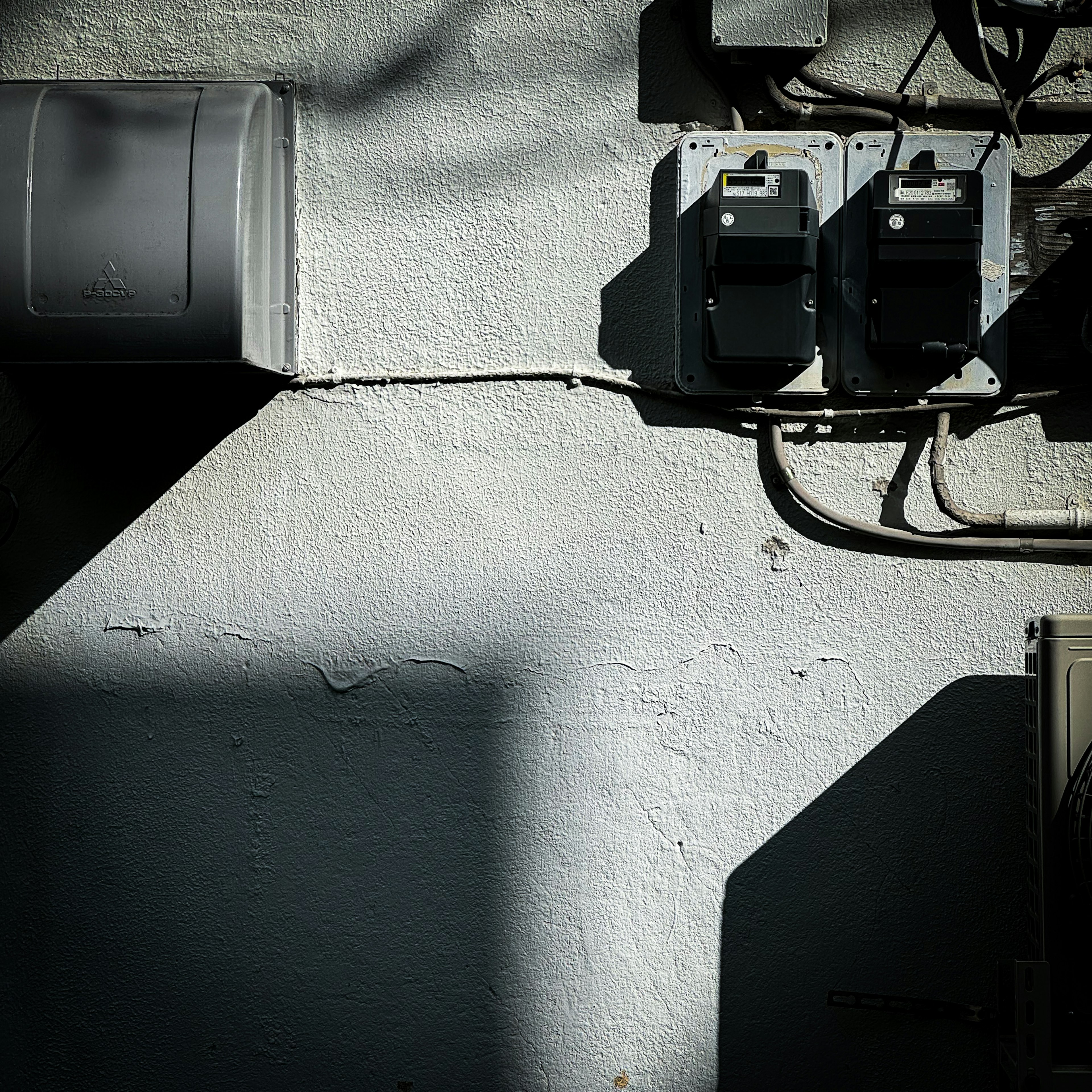 Electric meters mounted on a white wall with contrasting shadows