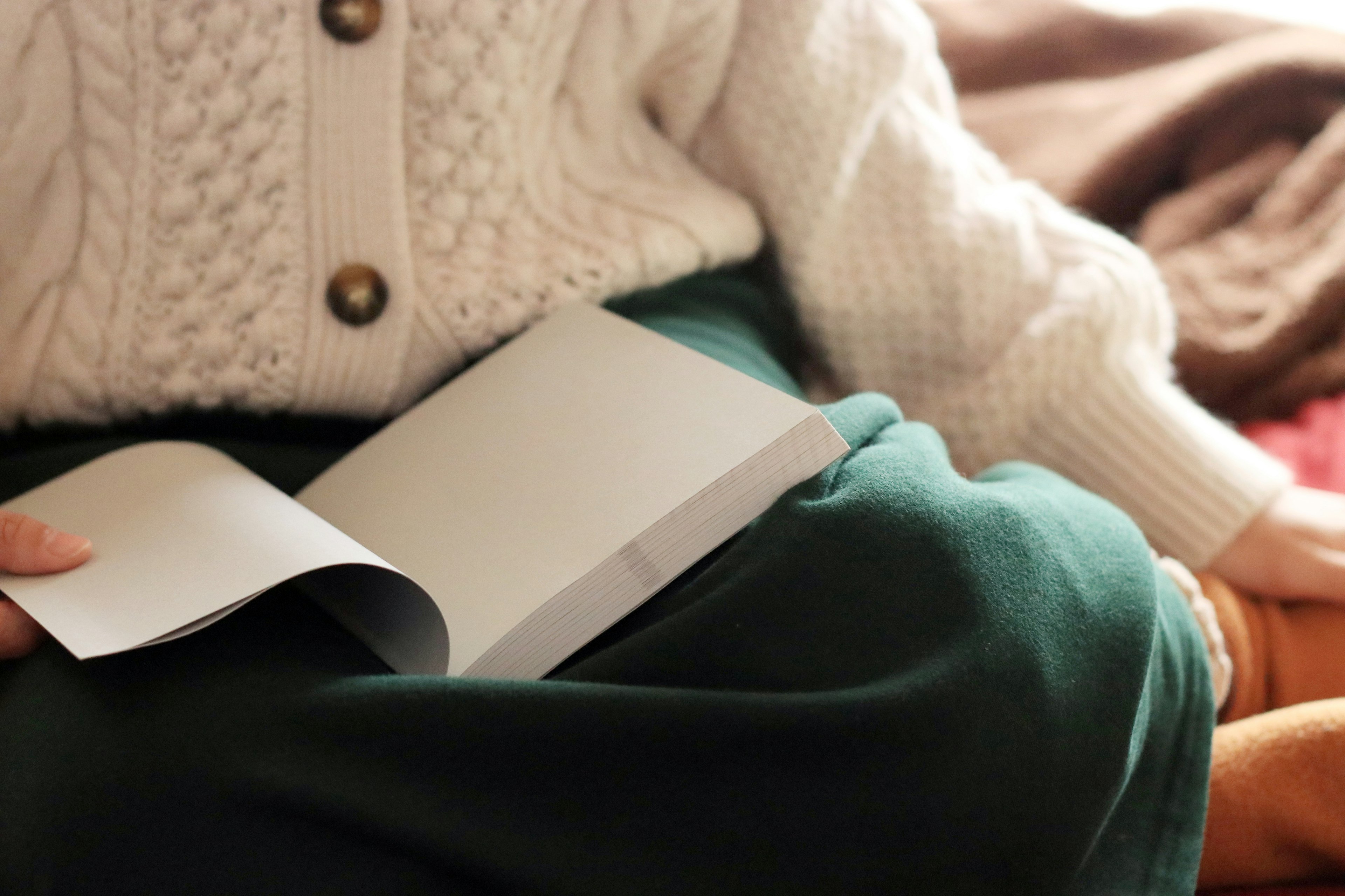 Persona con un maglione bianco seduta con una gonna verde che tiene un libro