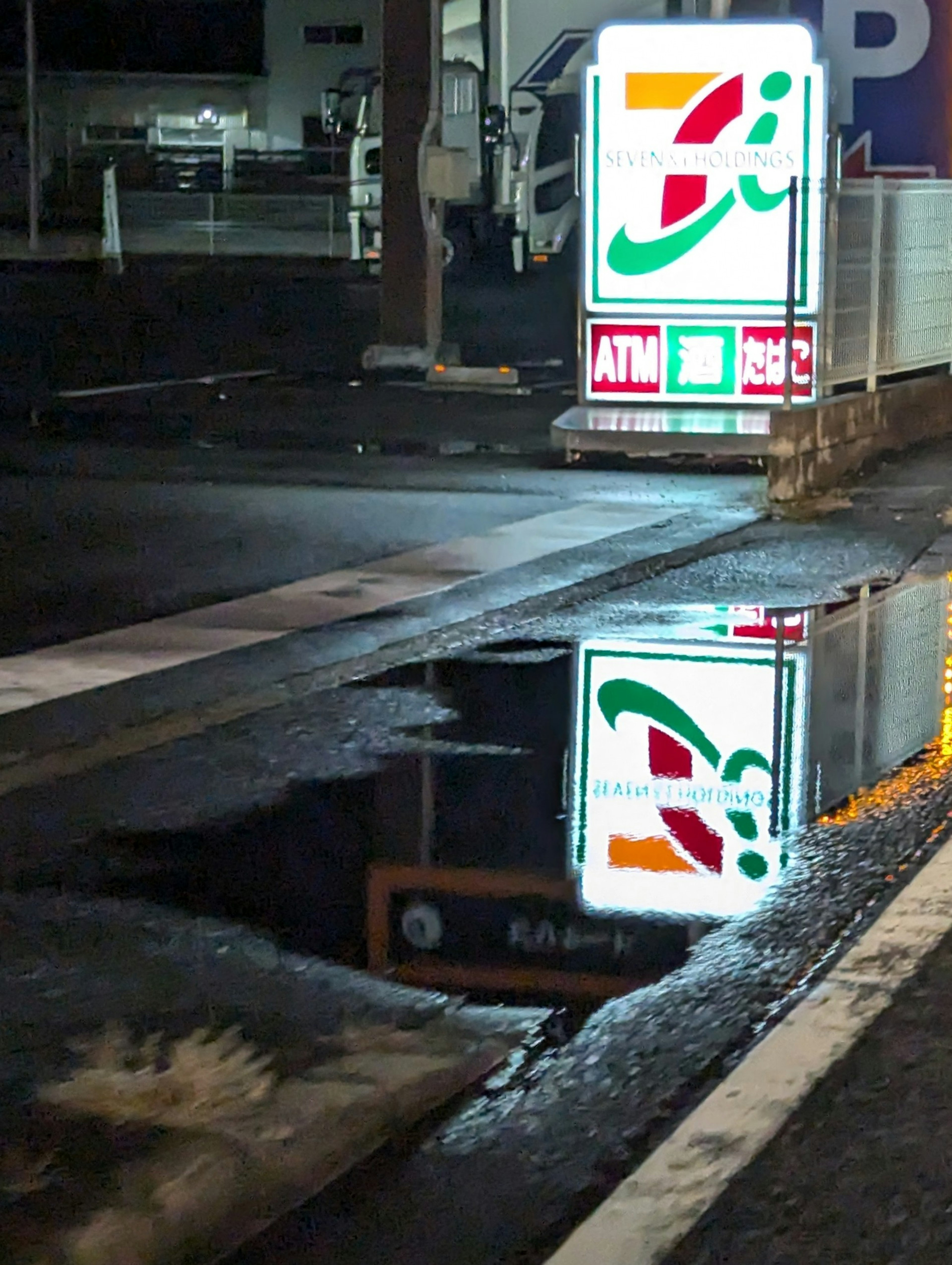 Refleksi papan 7-Eleven di genangan air pada malam hari