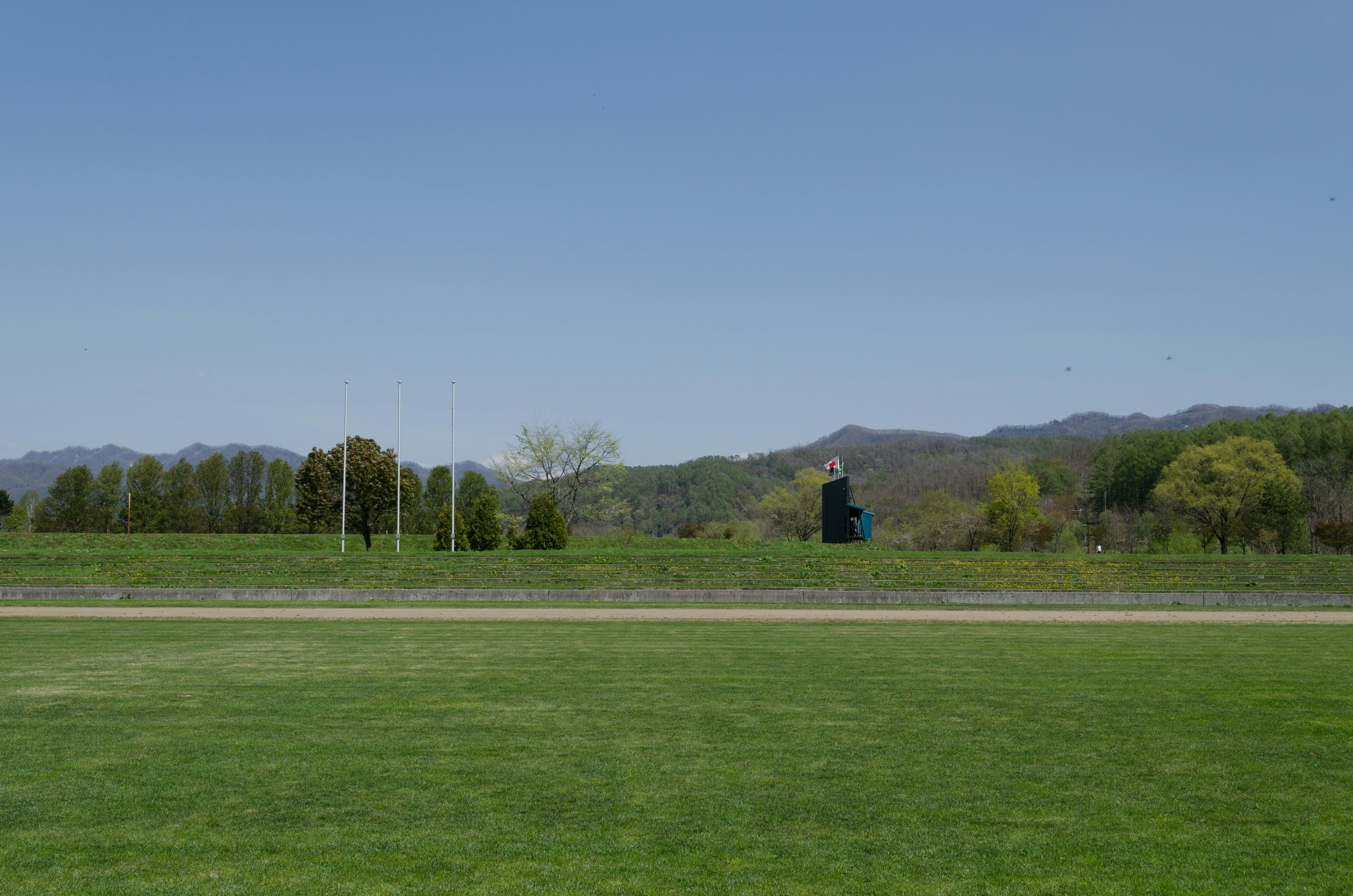 A landscape featuring a green field under a blue sky with distant mountains