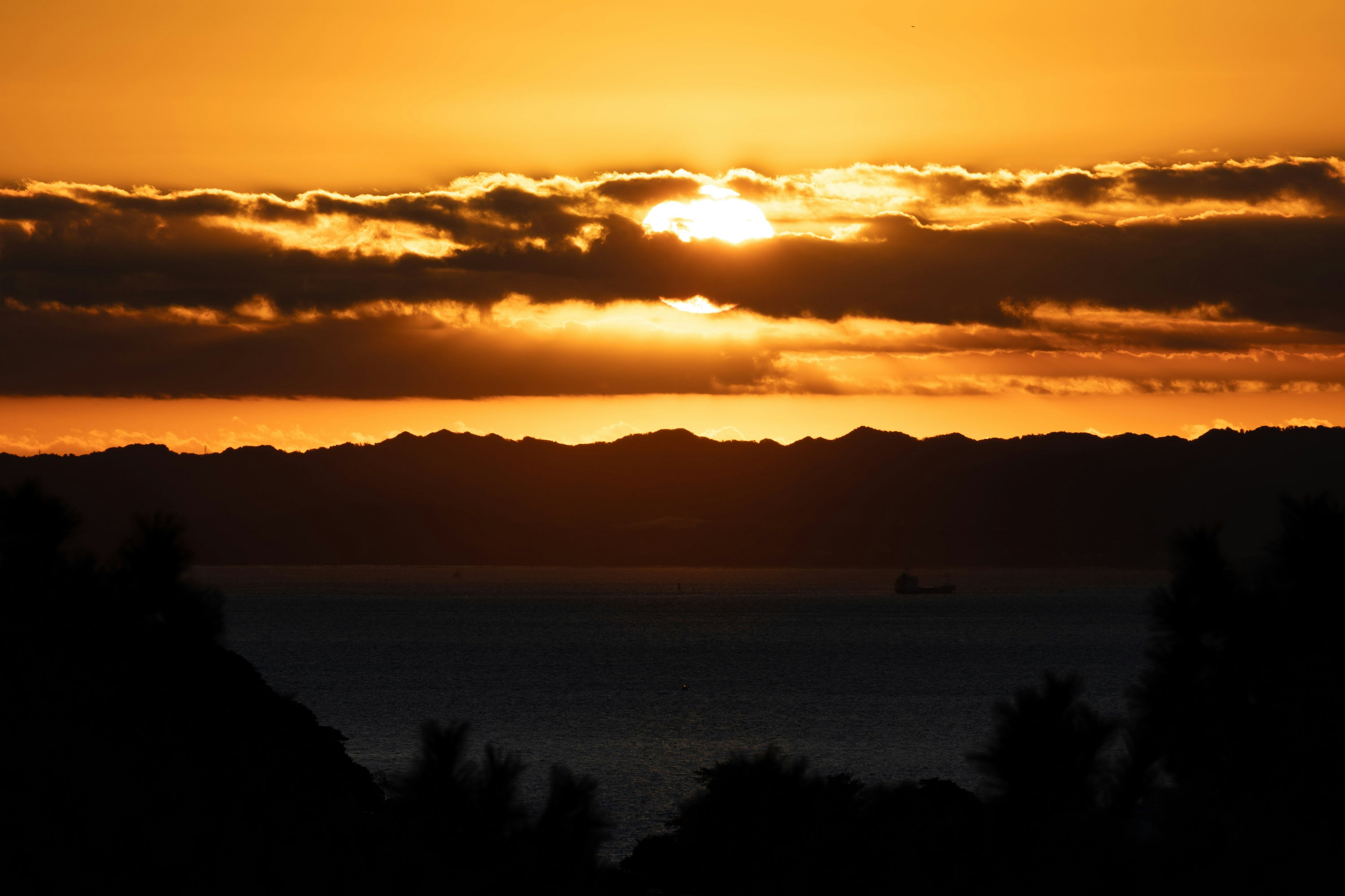 夕日が雲の間から昇る美しい風景 海と山のシルエットが見える