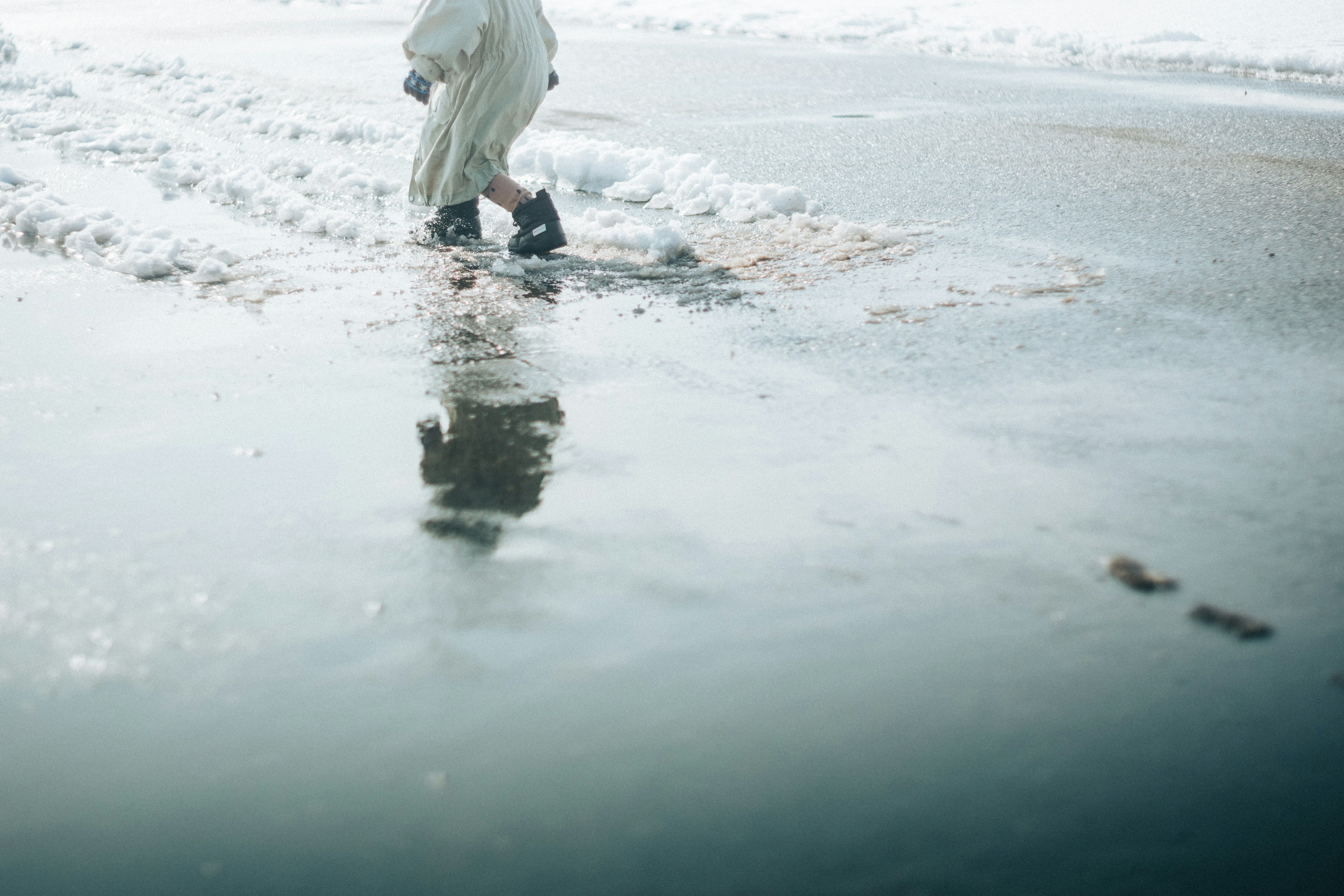 A person walking through a puddle reflecting in a winter landscape