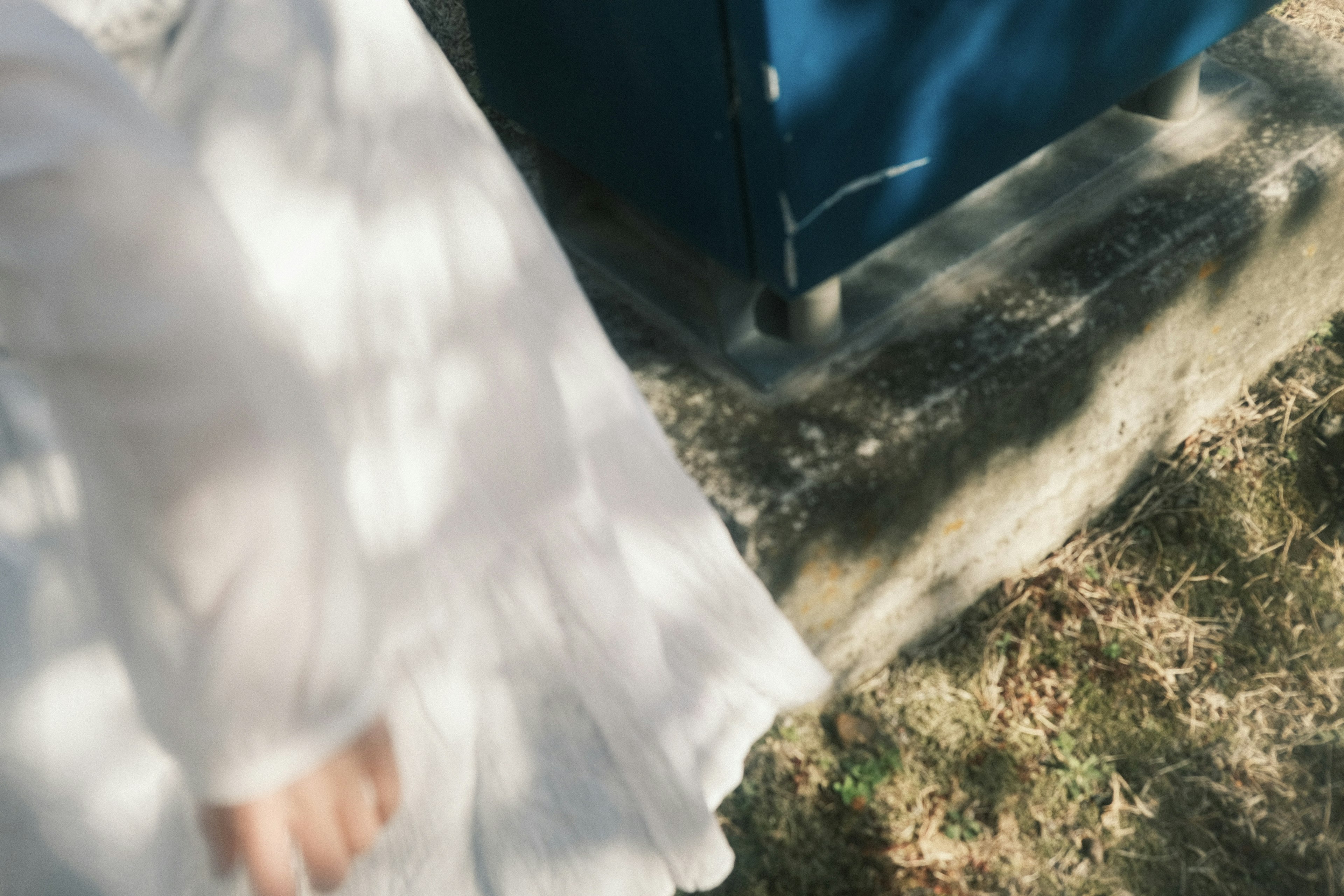 La mano de una mujer en vestido blanco cerca de la hierba y un objeto azul