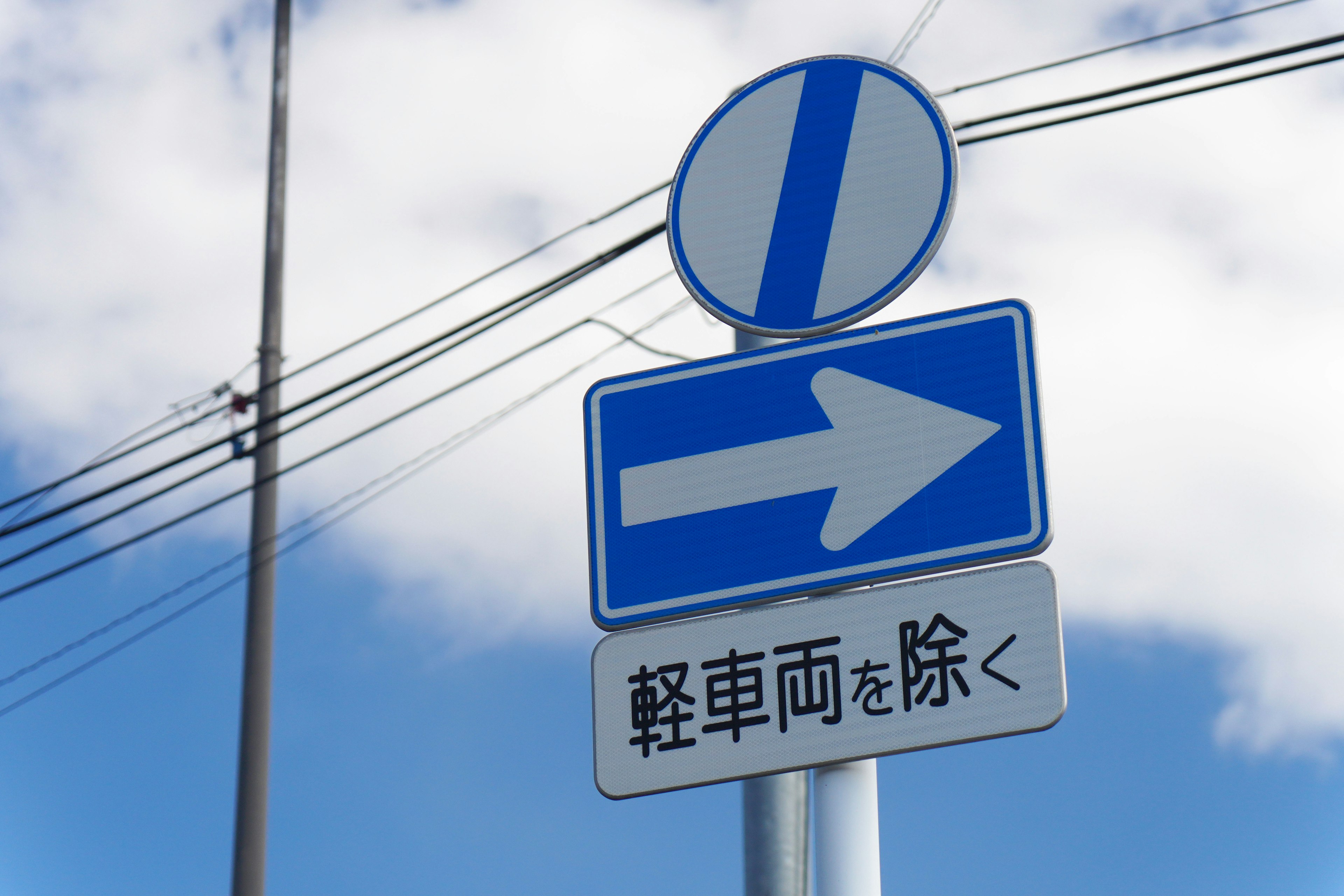 Blue directional traffic sign with an arrow and white background under a blue sky