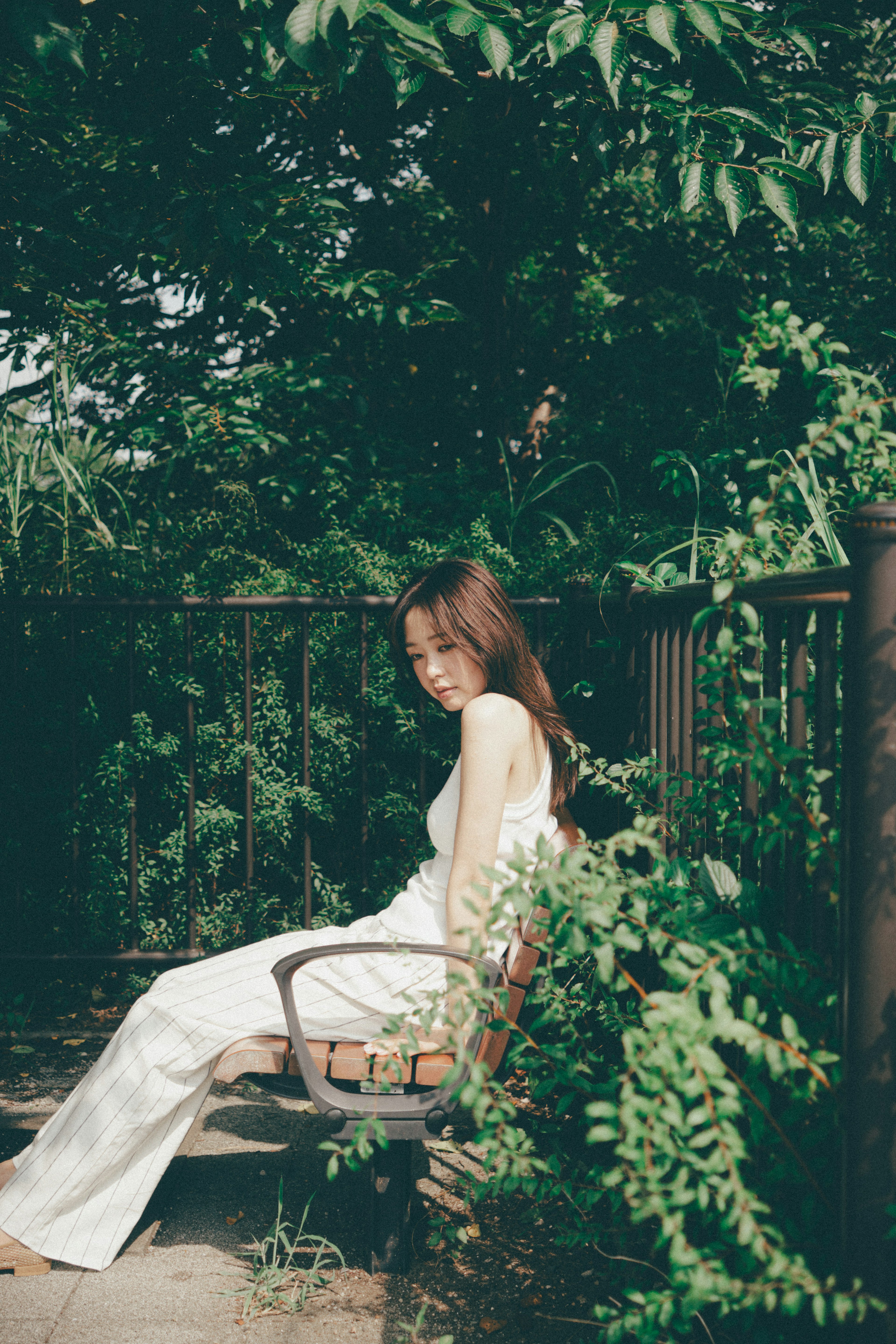 A woman in white clothing sitting on a bench surrounded by greenery