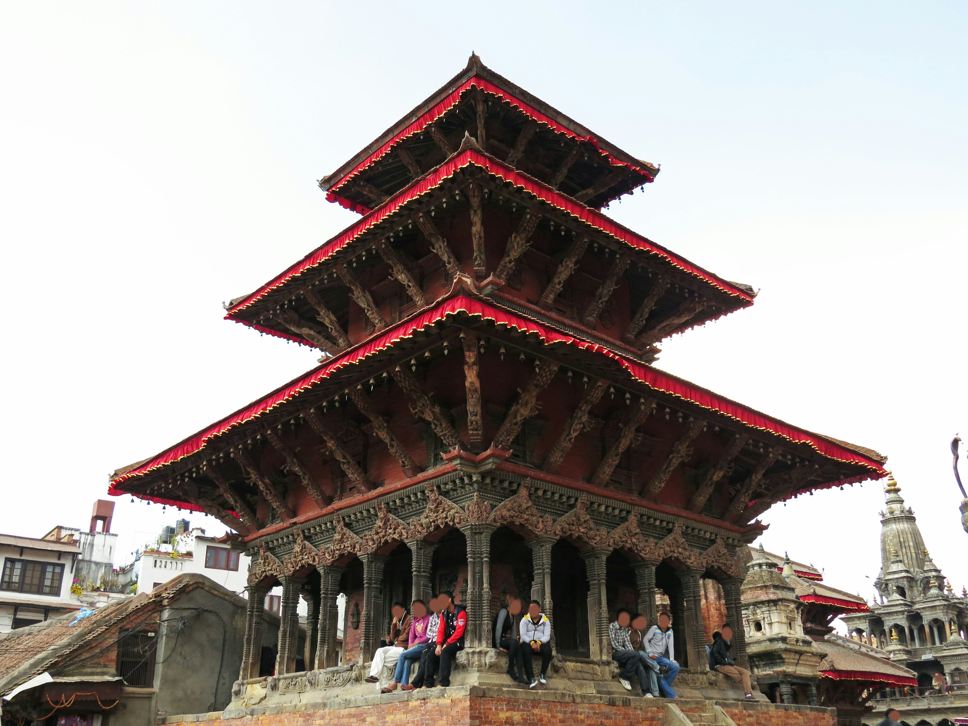 Traditional Nepali temple with three red roofs people seated around it