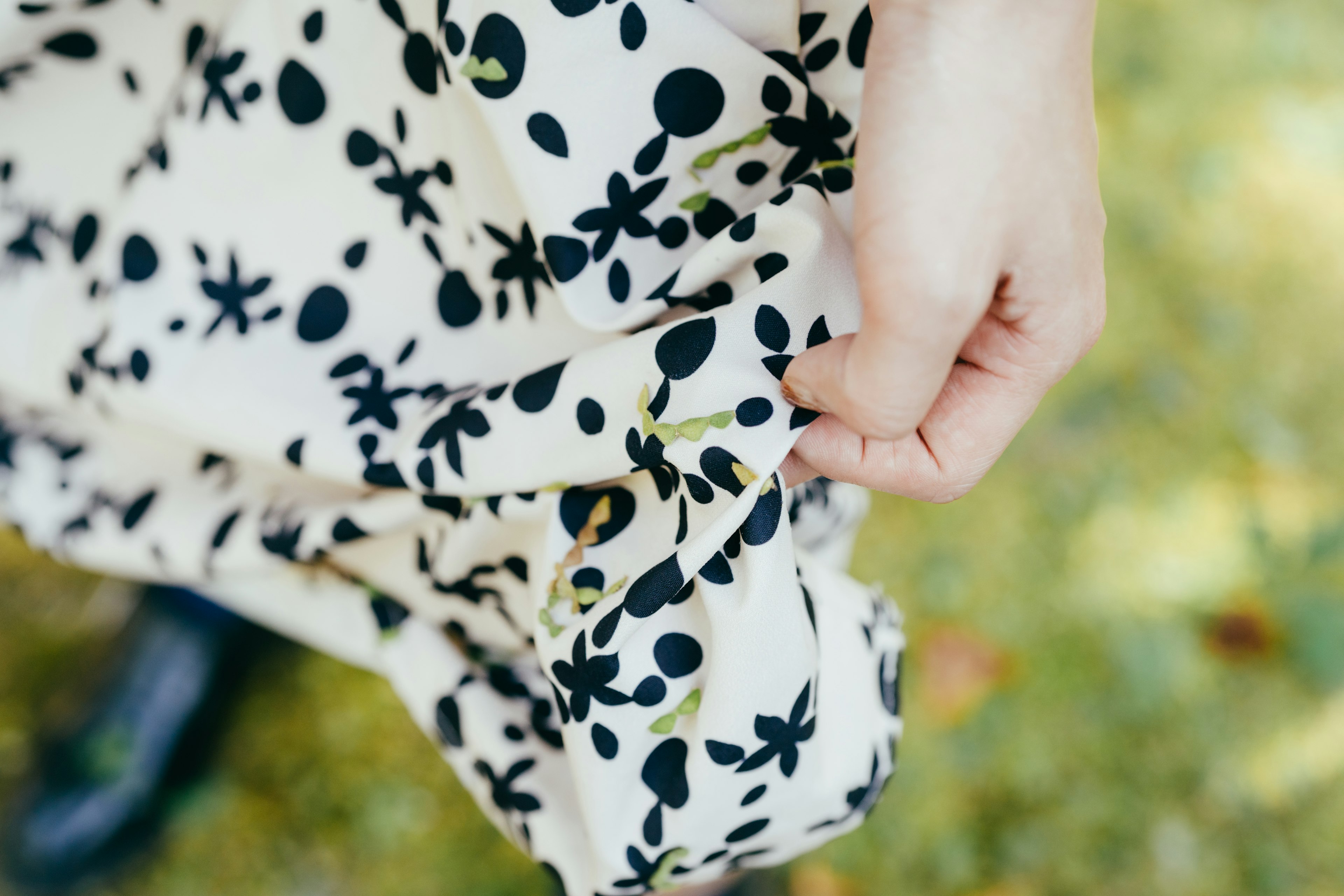 Hand holding a dress with black floral patterns on a white background