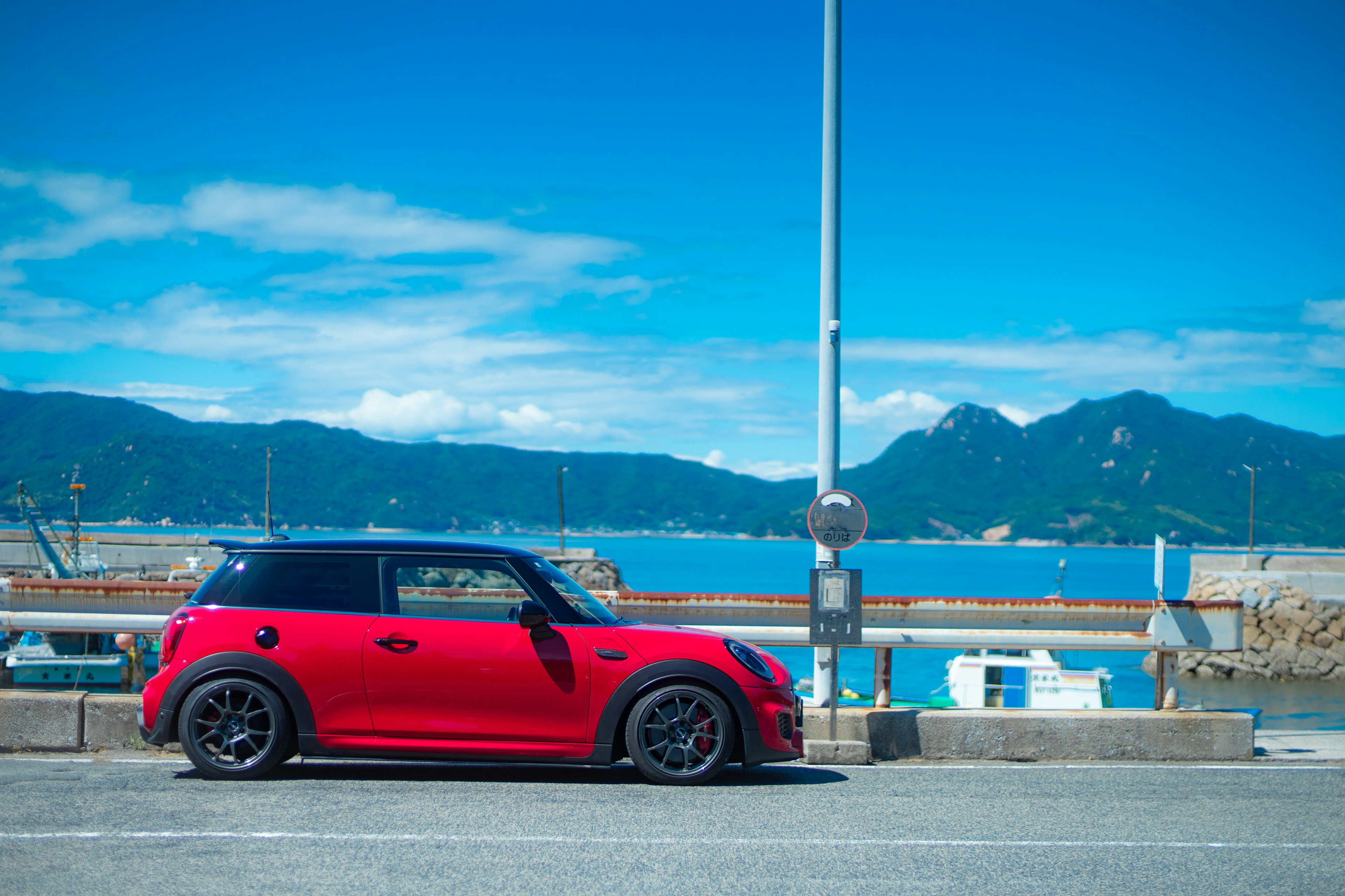 Red Mini Cooper parked by the seaside with a blue sky and mountains in the background