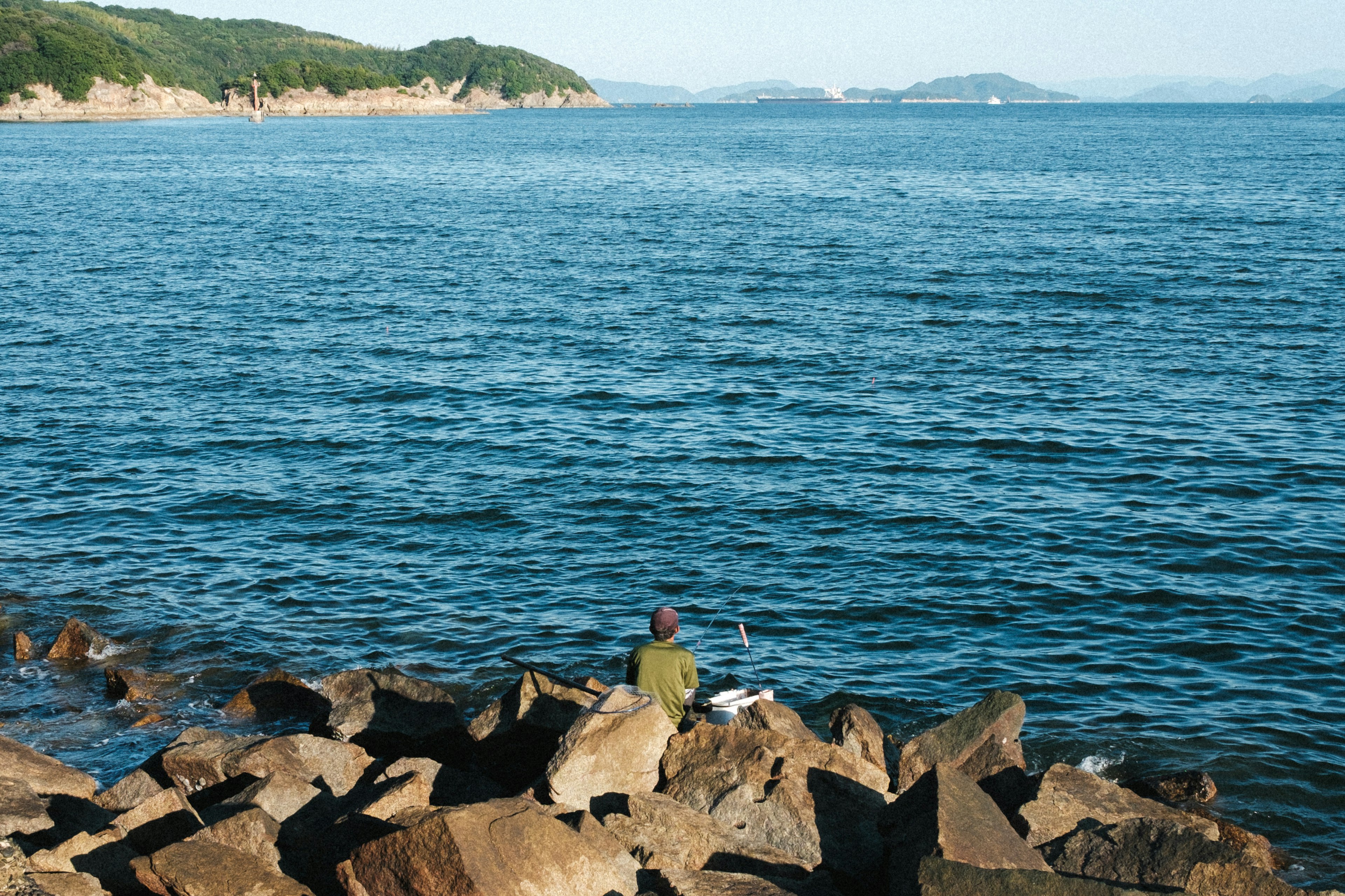 海辺の岩の上に座って釣りをする男性が映っている