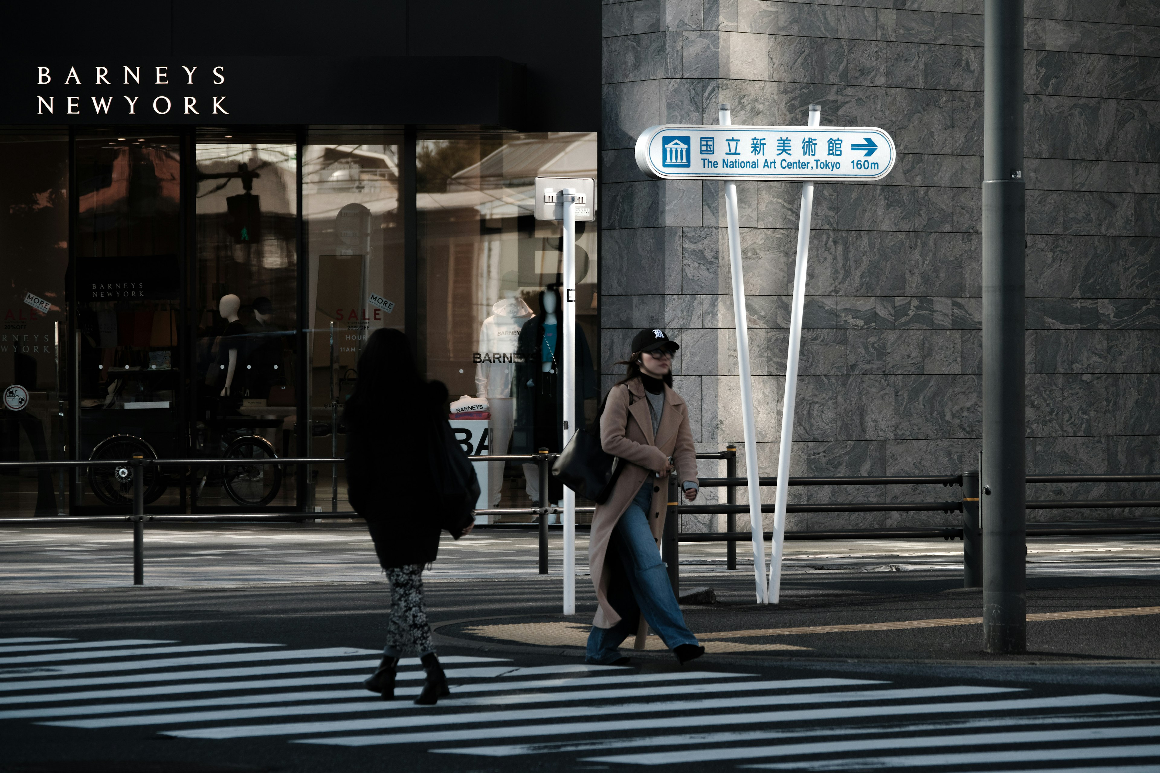 Two people crossing a street with a Barneys New York sign in the background