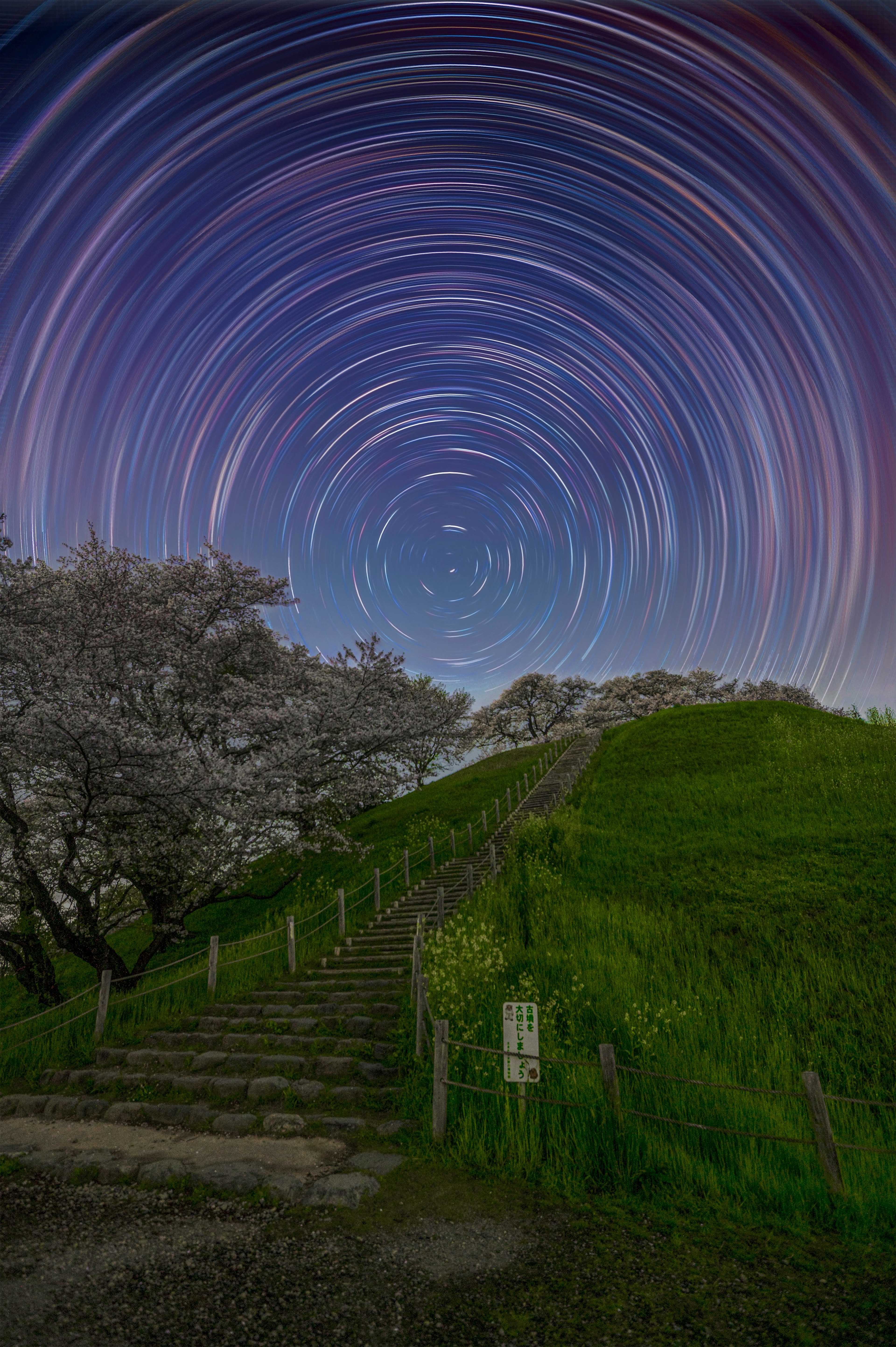 星の軌跡が描かれた夜空と階段のある緑の丘の風景