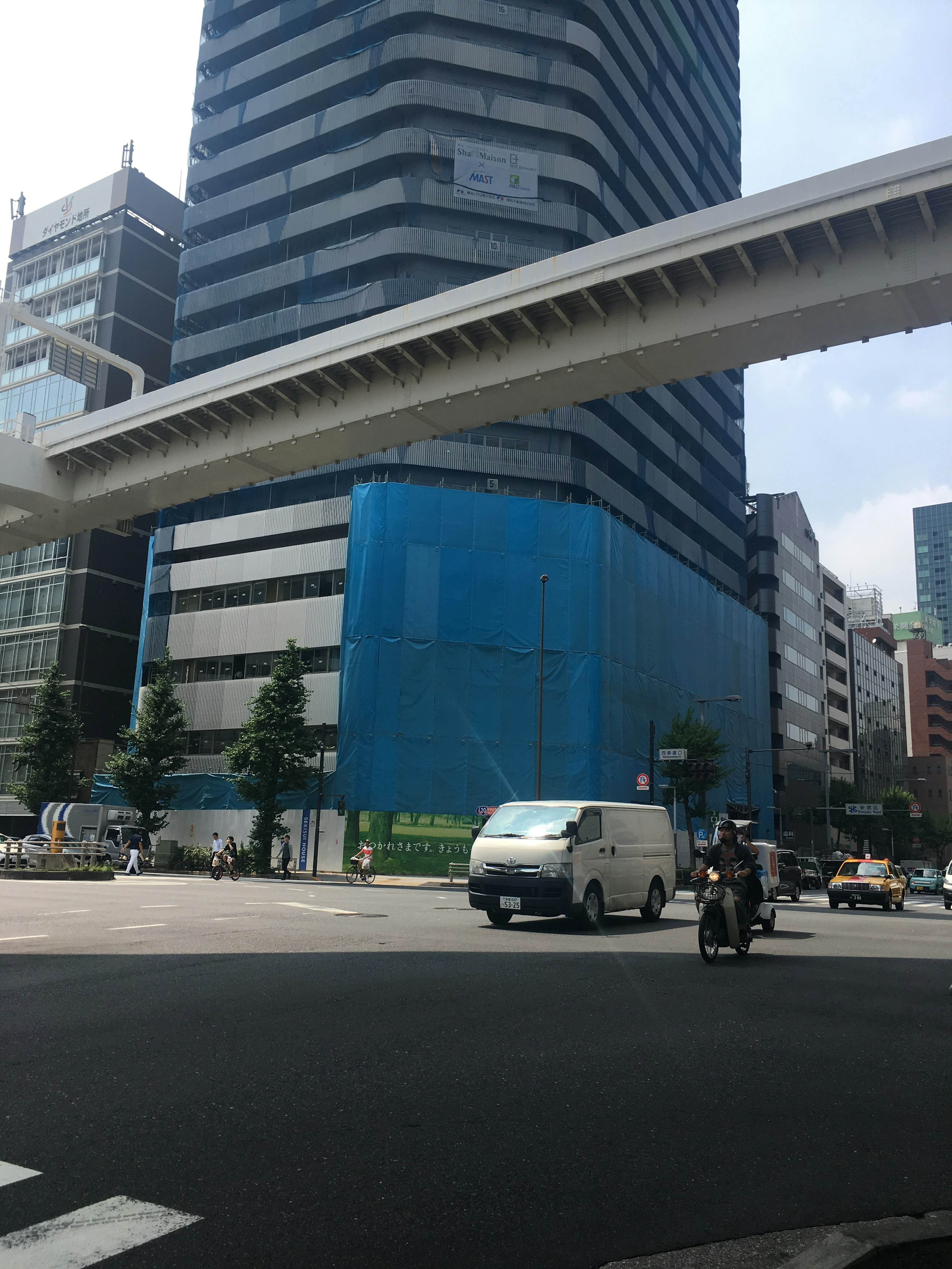 Bauplatz mit blauer Plane um ein Hochhaus und Verkehrsszene