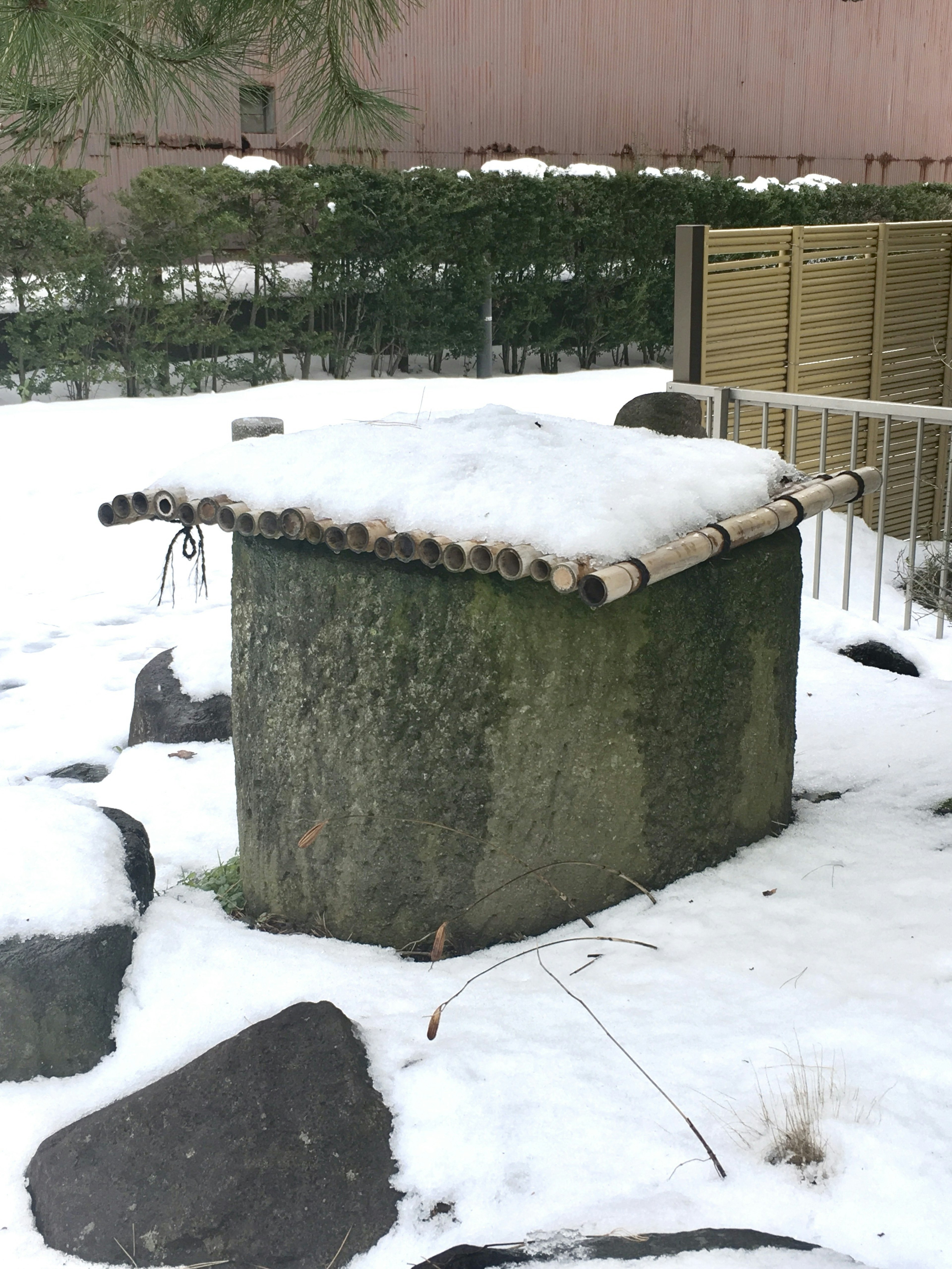 Stone box covered with snow and wooden roof in a garden setting