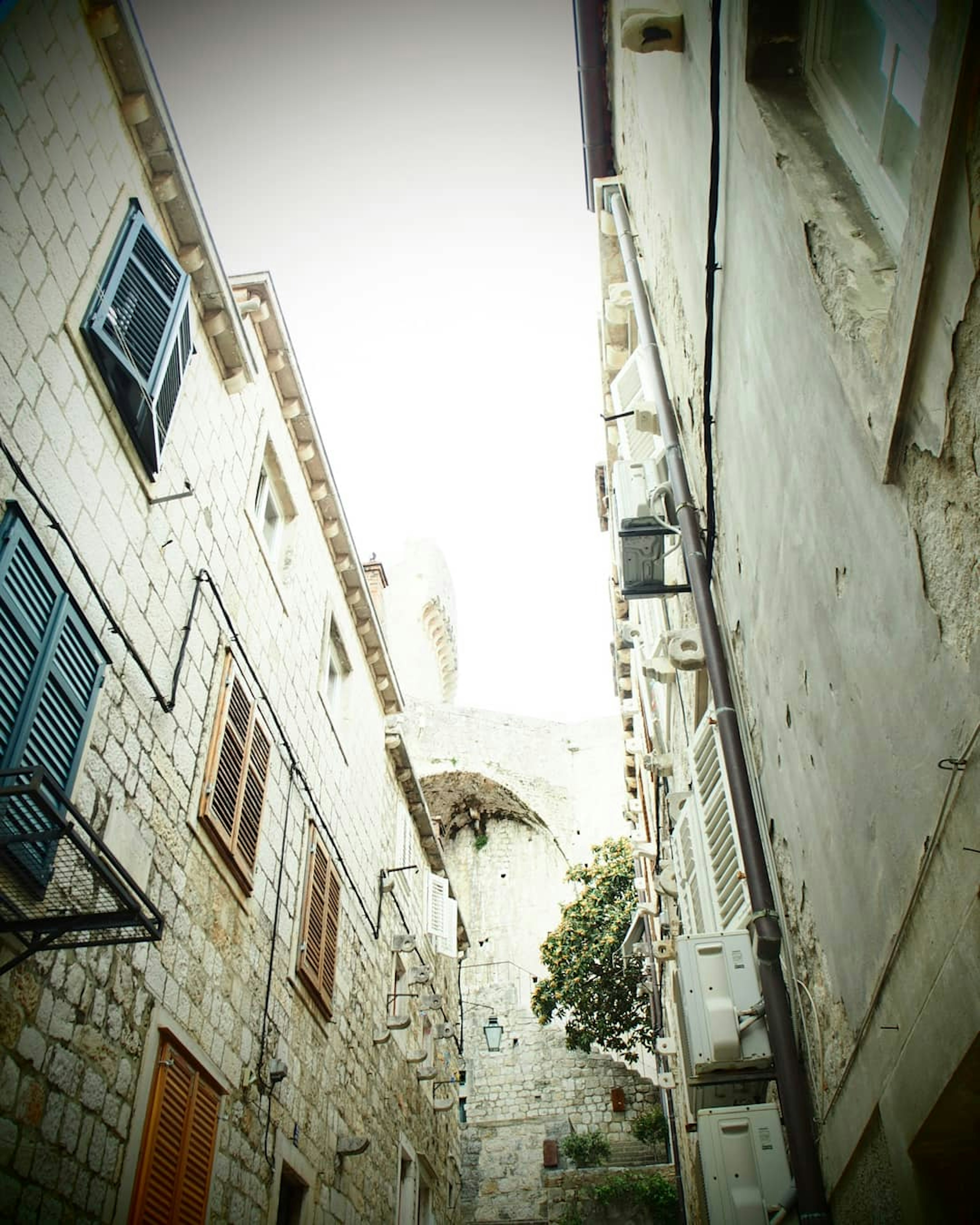 Vista hacia arriba de un callejón estrecho de piedra con edificios antiguos y ventanas