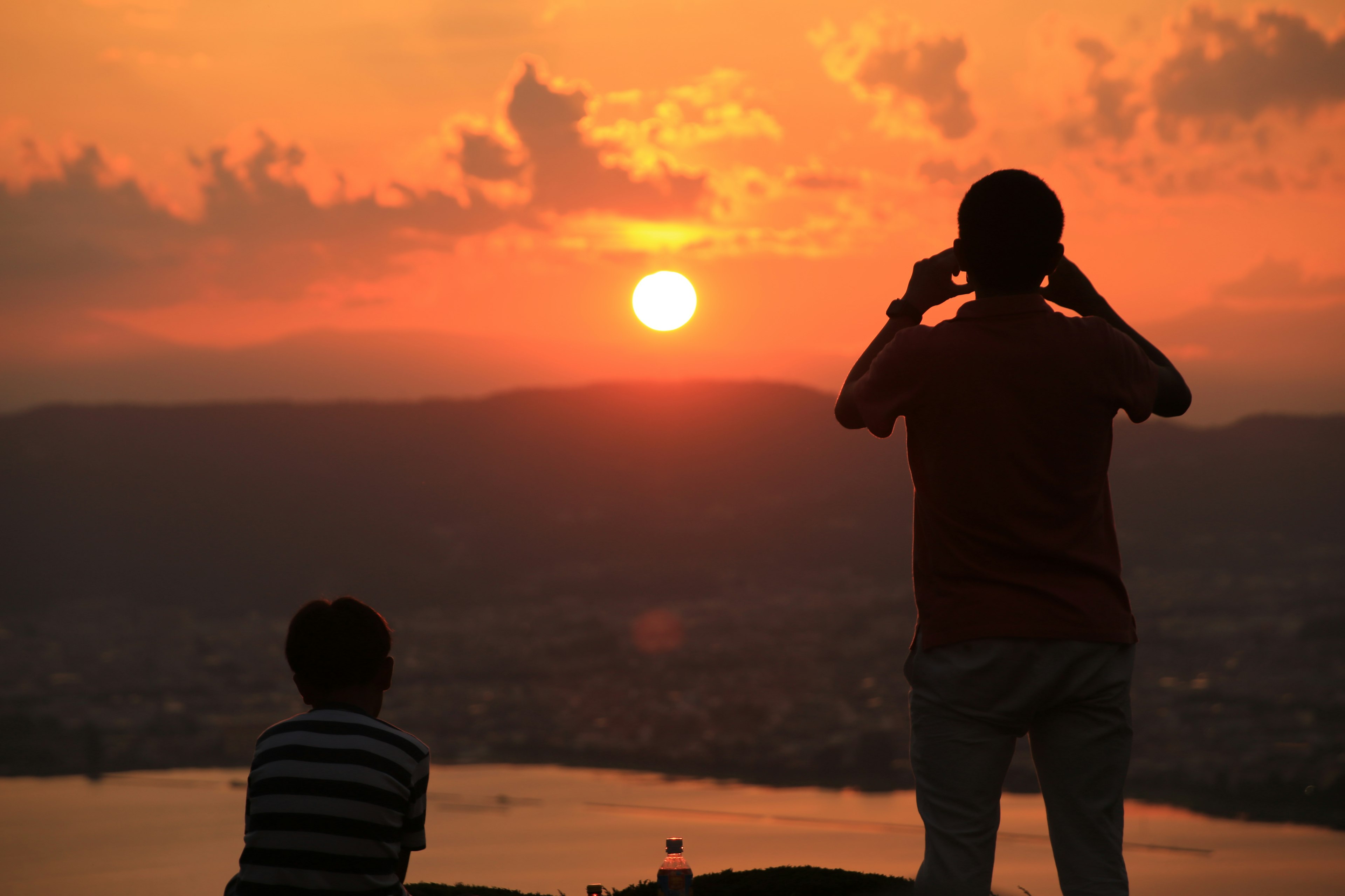 Silhouette eines Elternteils und eines Kindes, die den Sonnenuntergang mit einem schönen orangefarbenen Himmel beobachten