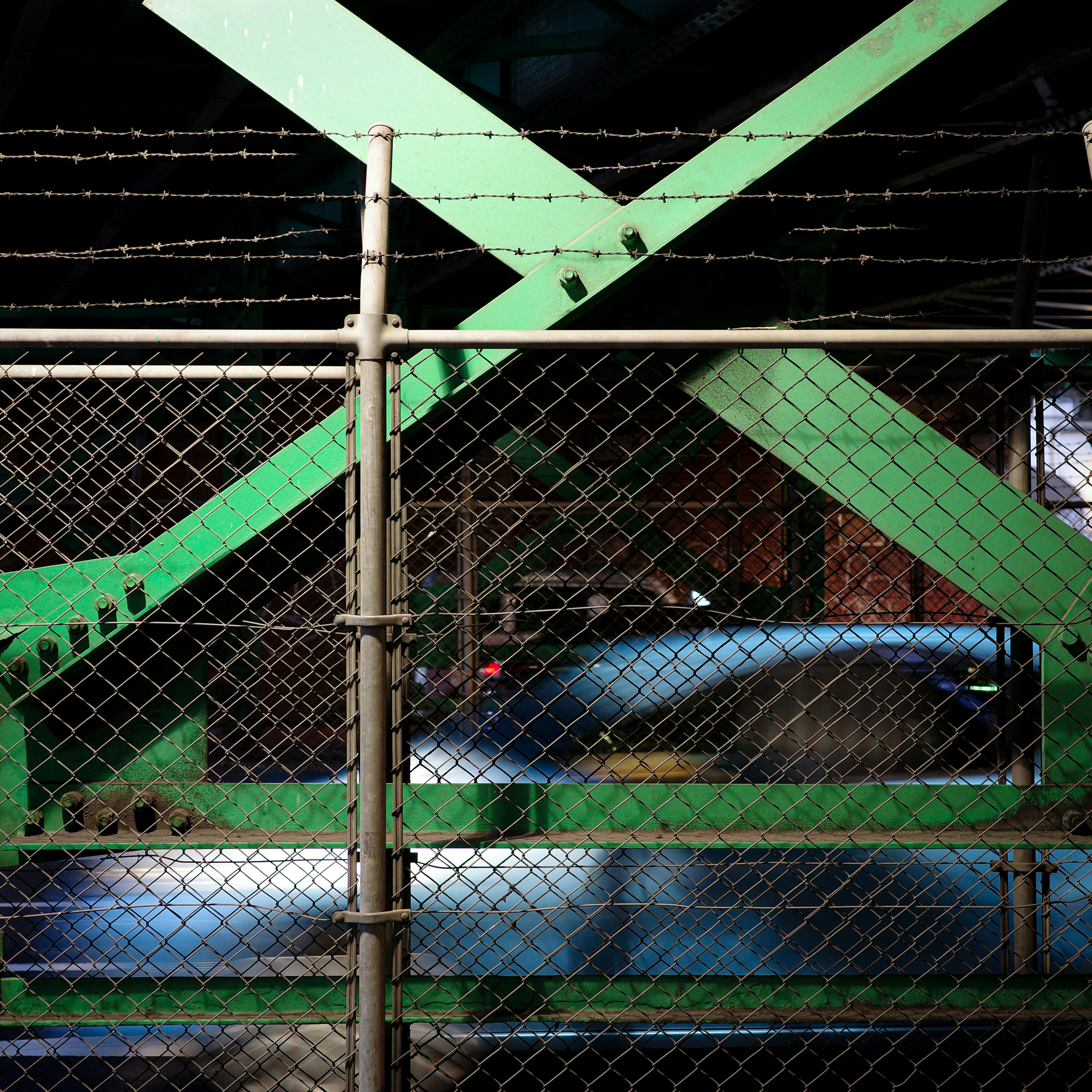 Image showing a flowing car seen through green steel beams and a fence