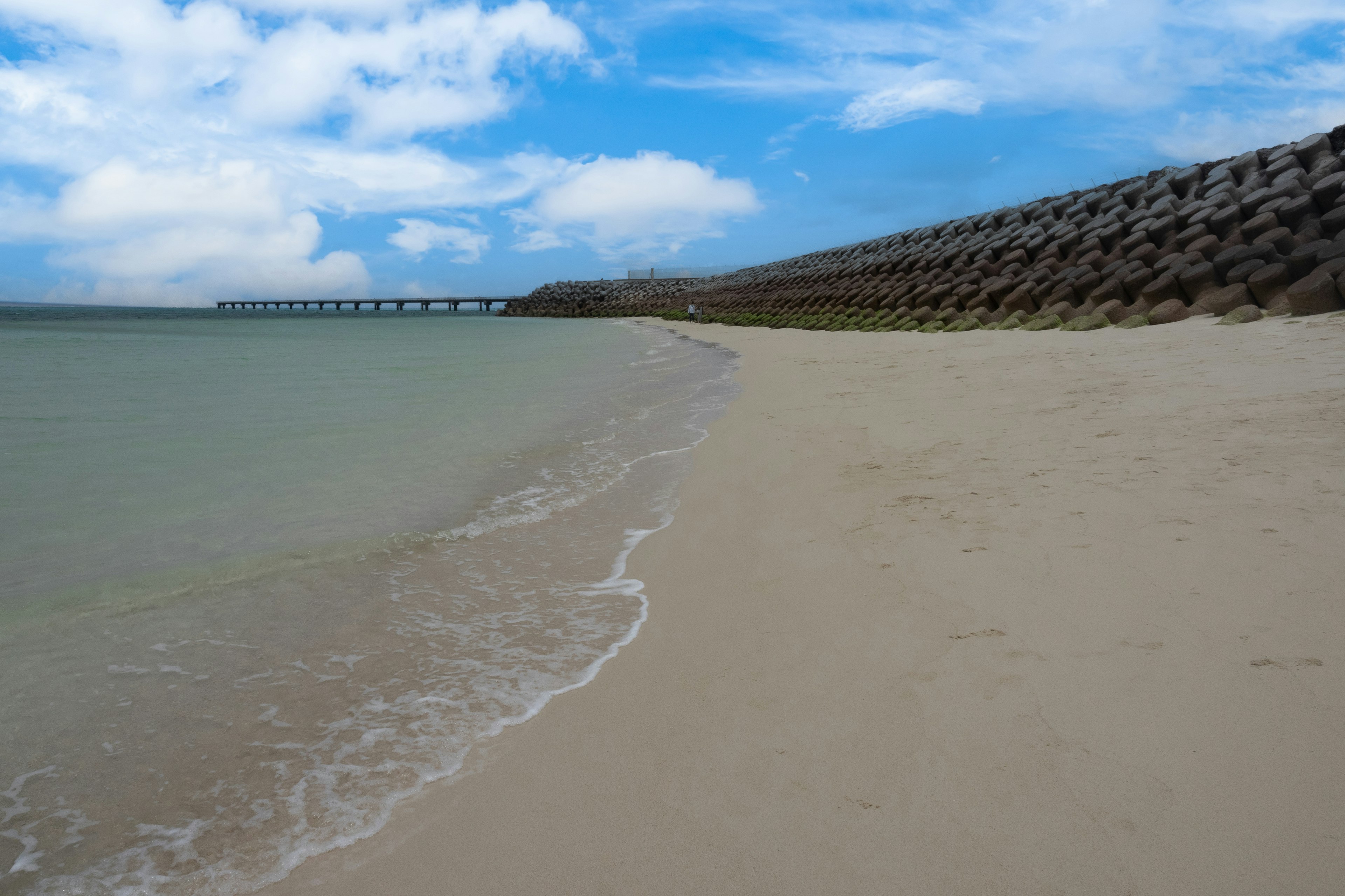 Scenic beach view with blue sky and calm sea featuring sandy shore and breakwater