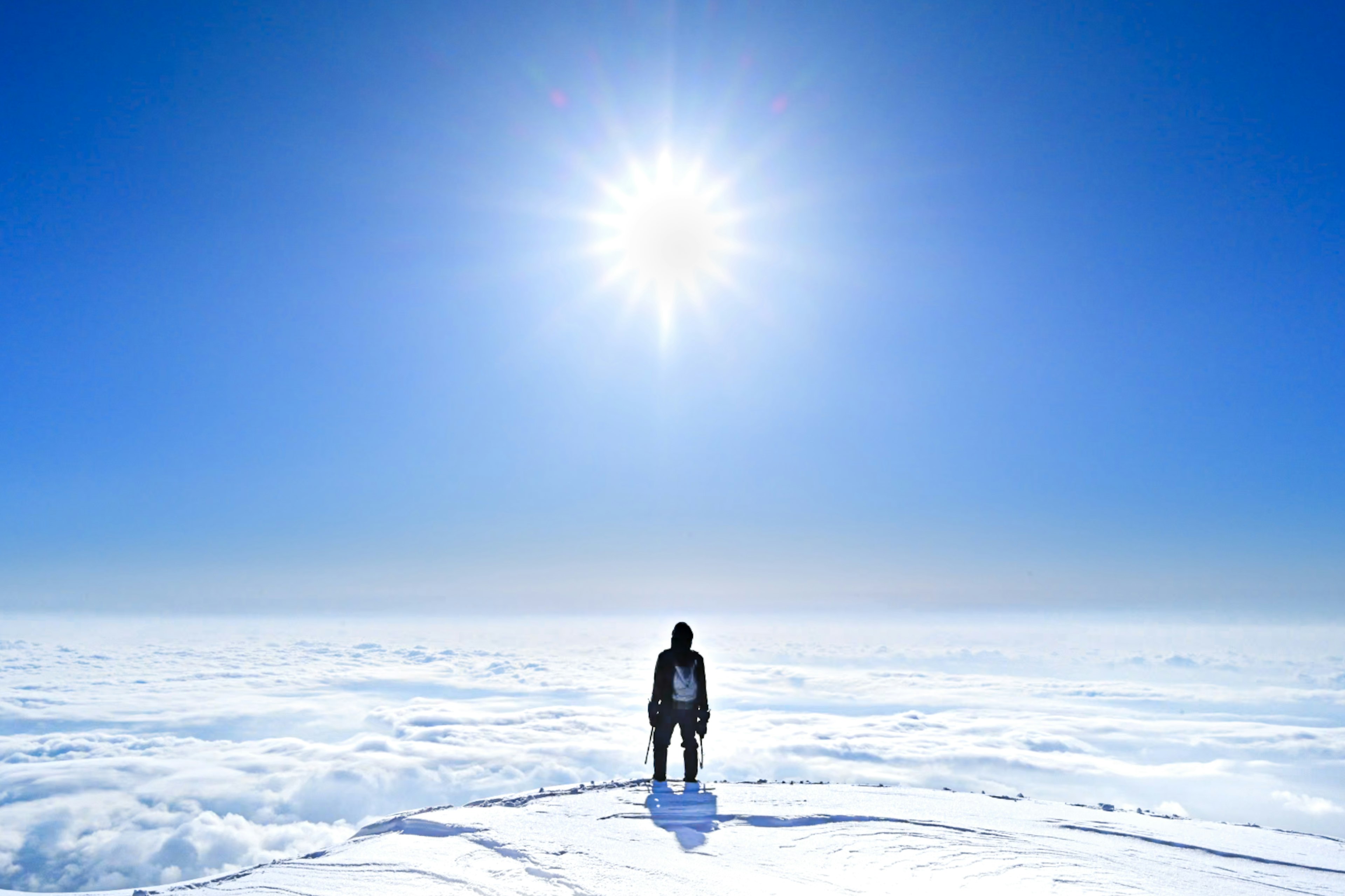 Person steht auf Schnee mit hellem Sonnenlicht und klarem blauen Himmel