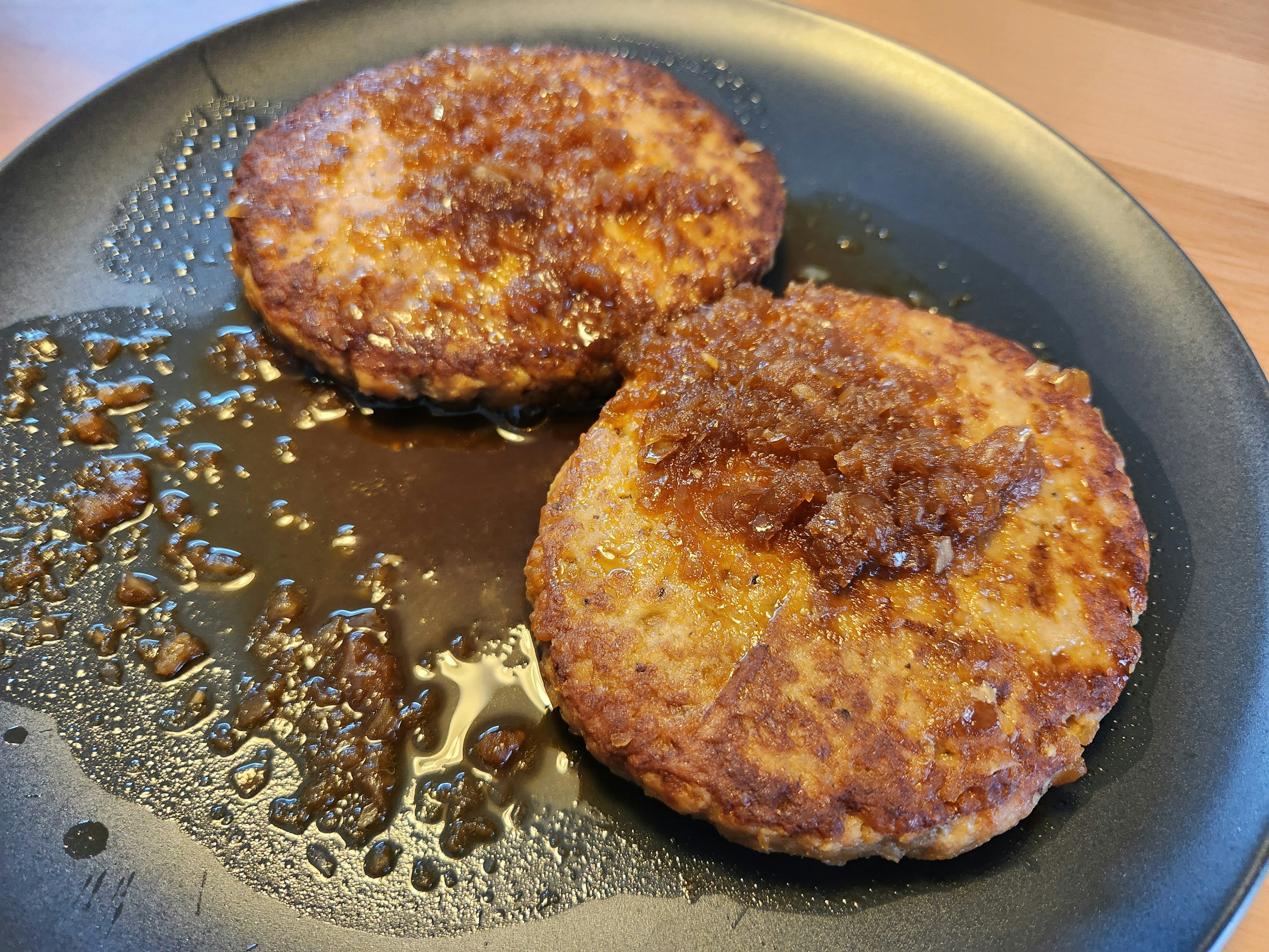 Dos croquetas recién fritas en un plato negro con salsa dulce