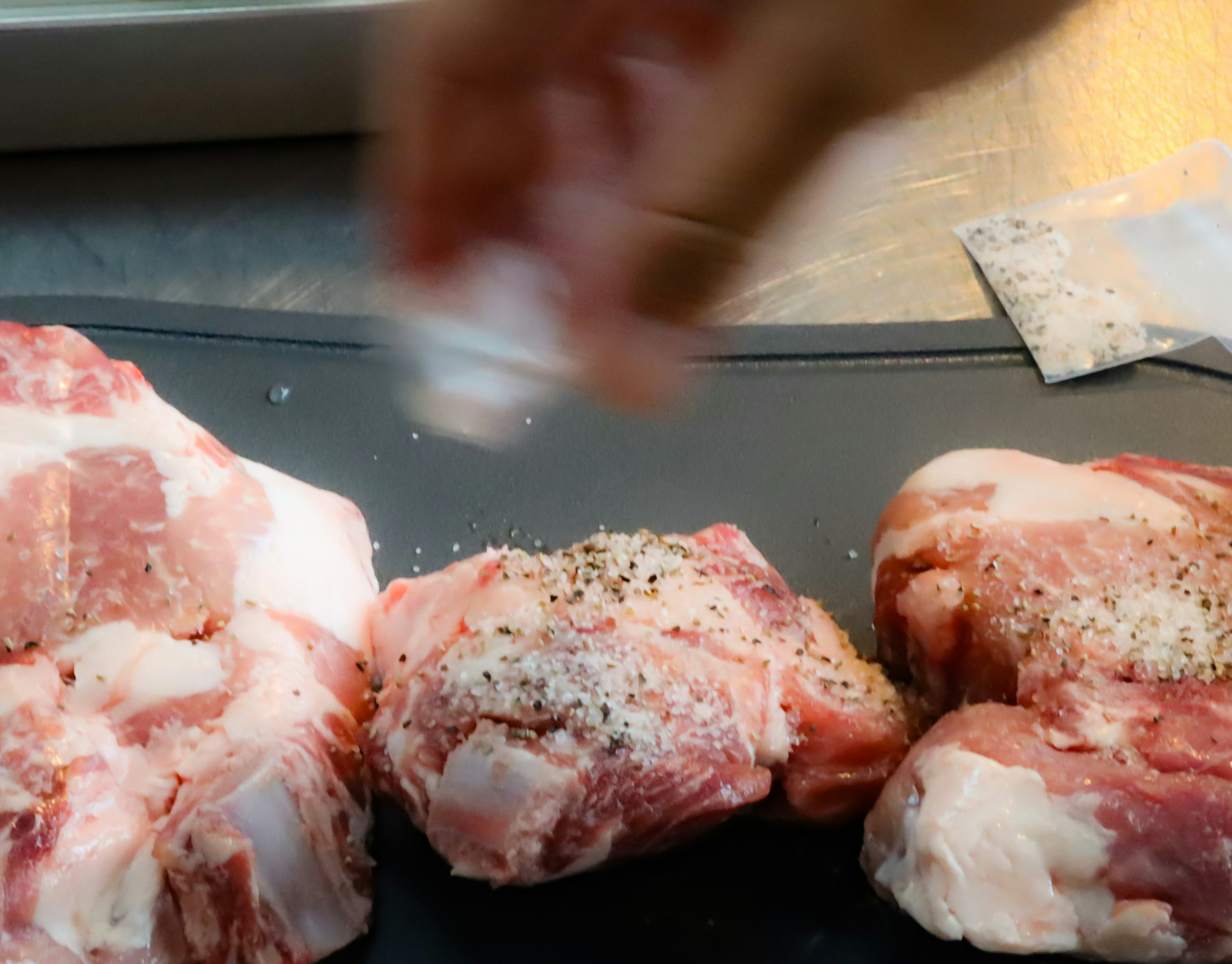 Hand sprinkling salt and pepper on meat cuts