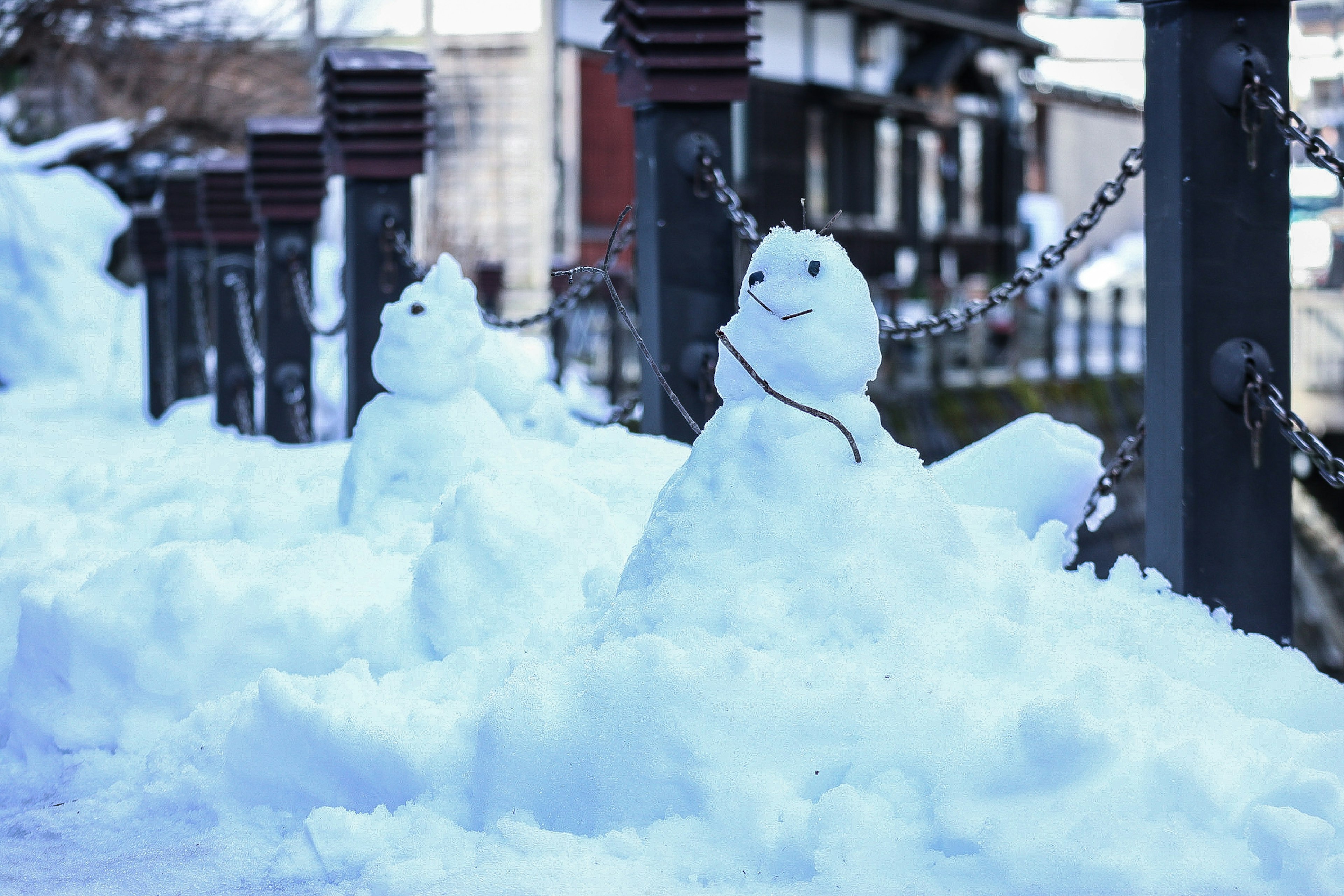 Snowmen in a snowy landscape with buildings in the background